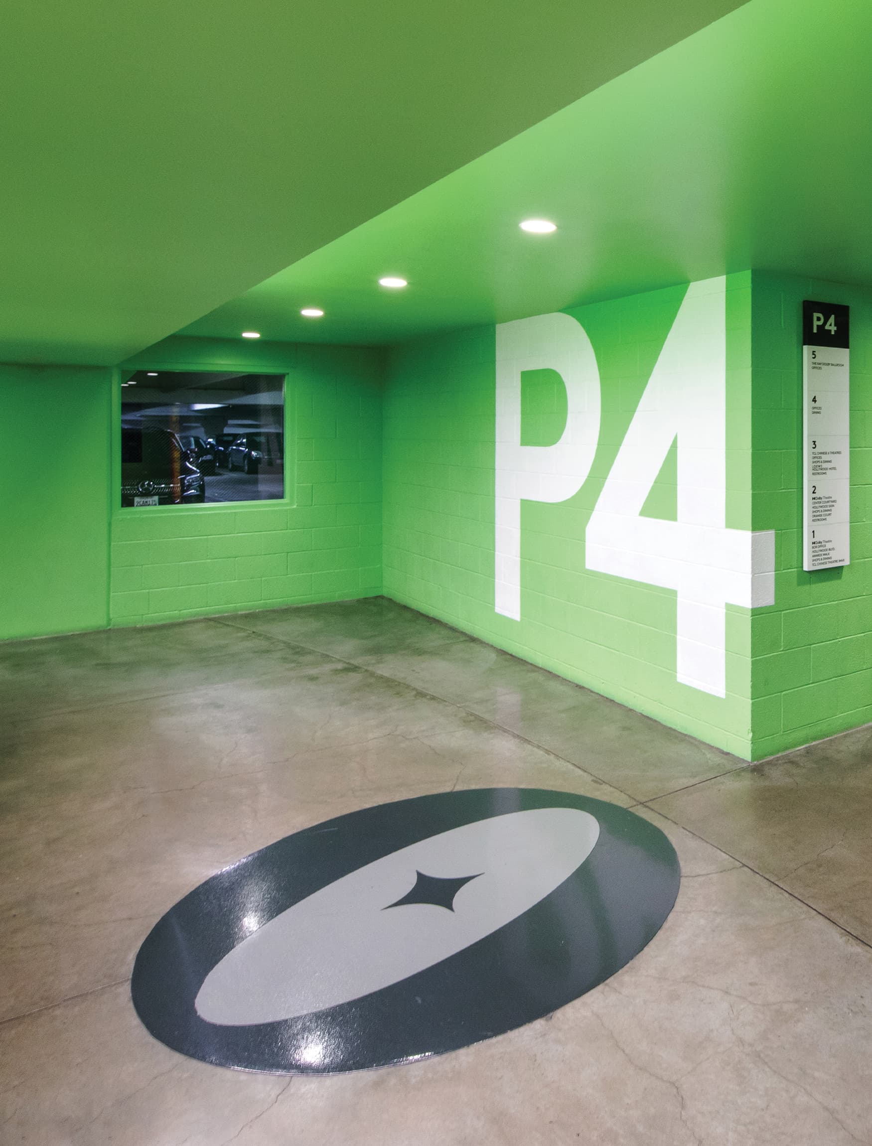Image of large painted parking garage level identity in white wrapping corner to a wall mounted elevator directory of levels with black and white graphics and a painted Ovation Hollywood "O" icon logo on the ground by RSM Design for Ovation Hollywood in Los Angeles, California.