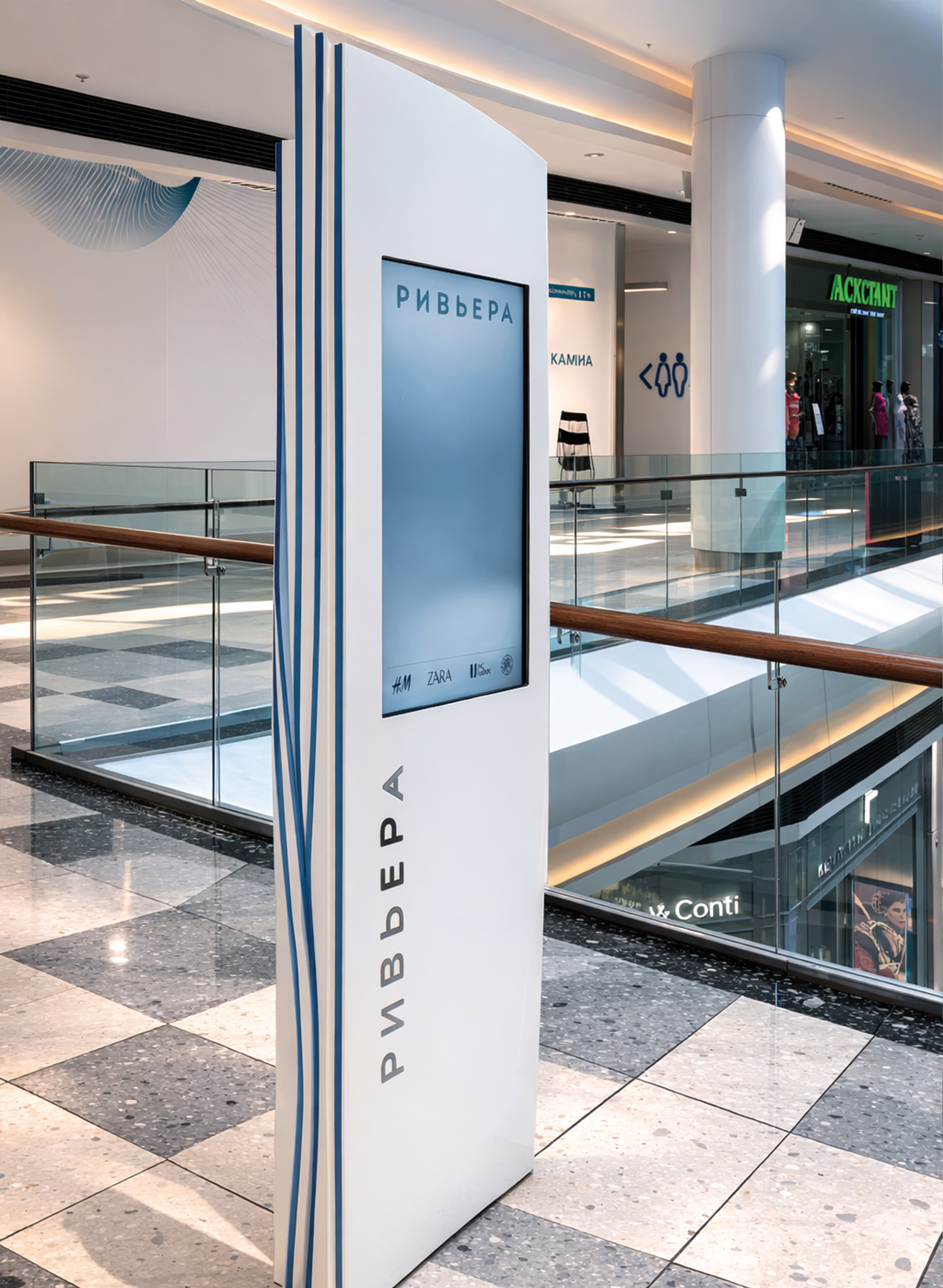 Branded digital wayfinding kiosk with integrated display screen and vertical Cyrillic identity lettering in the interior concourse of Riviera international retail and mixed-use destination — RSM Design digital integration, wayfinding and signage design, master sign programs, and environmental graphic design for retail, mixed-use, and international destinations.