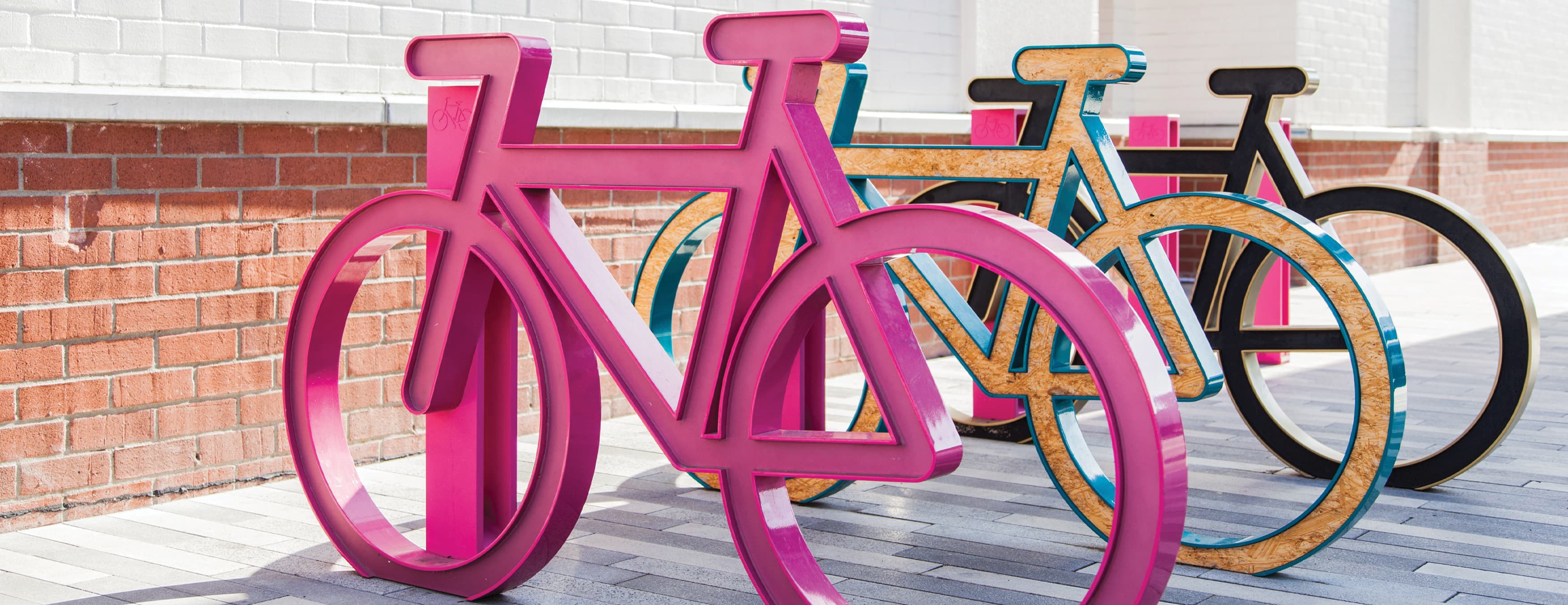 Sculptural artistic bike rack with large metal bikes in pink, blue and black colors with brick wall in the background