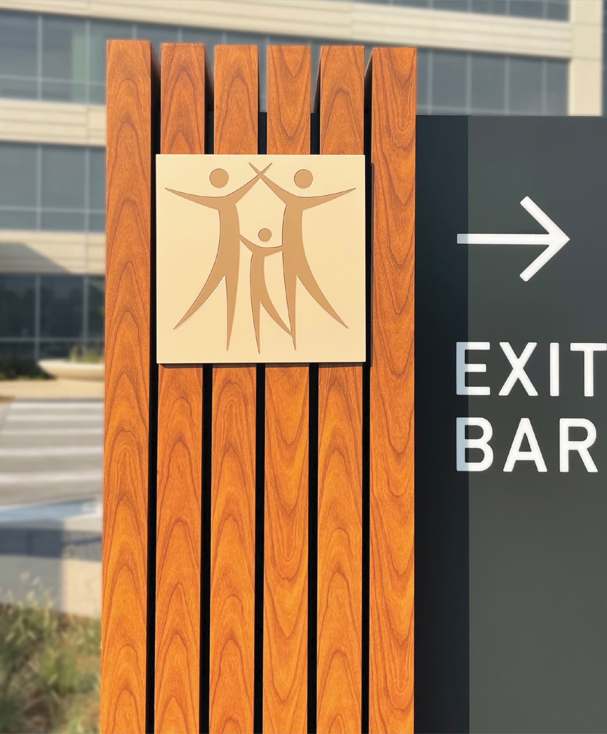 Close-up detail of a custom healthcare wayfinding sign featuring vertical wood slats, a dimensional emblem panel, and integrated directional graphics within a contemporary campus setting. This exterior environmental graphic design solution reflects RSM Design’s expertise in comprehensive wayfinding systems for healthcare, mixed-use, and commercial developments.
