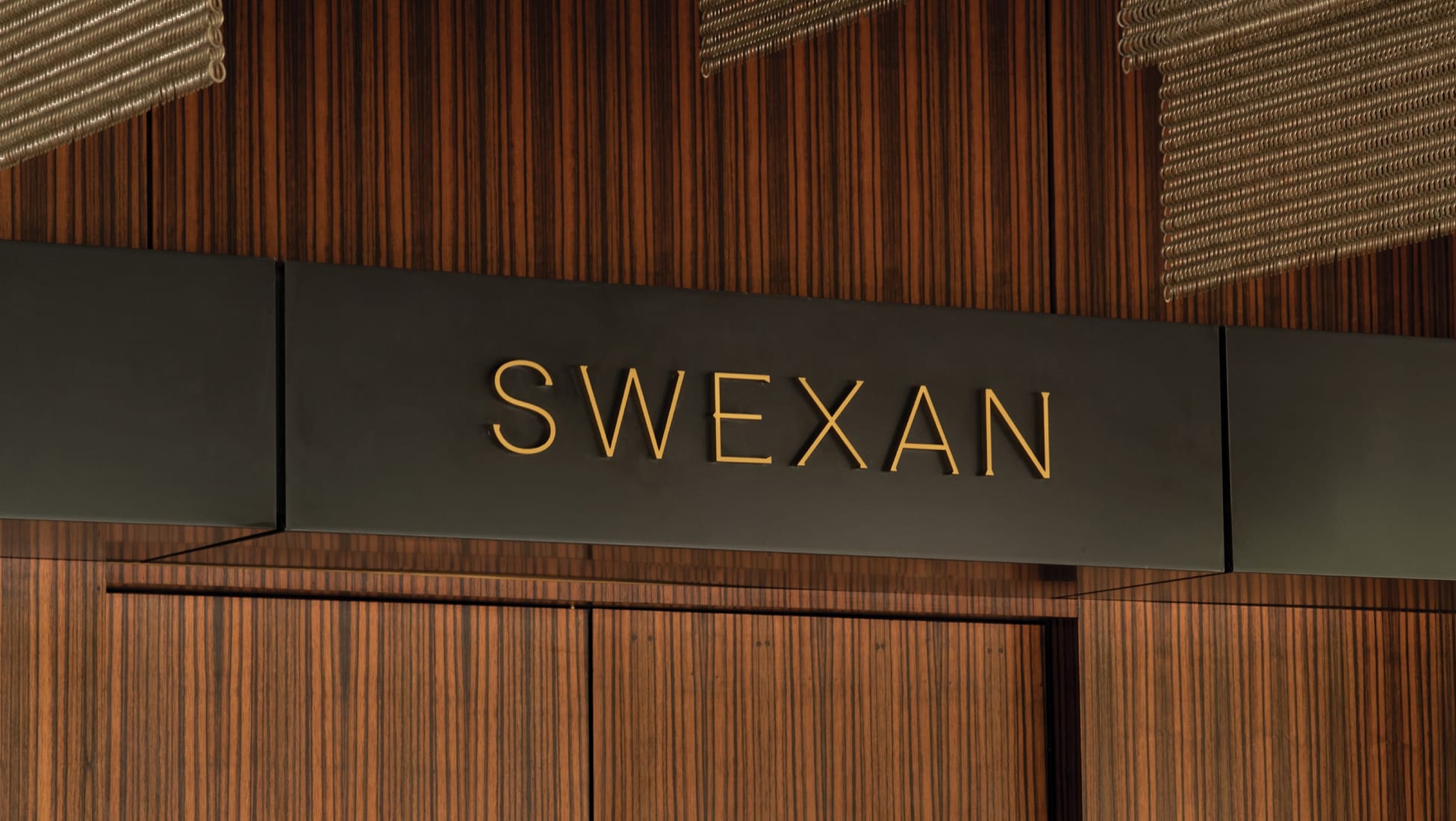 Gold dimensional "Swexan" sign on a wood-paneled entrance at The Swexan Hotel - environmental graphic design by RSM Design