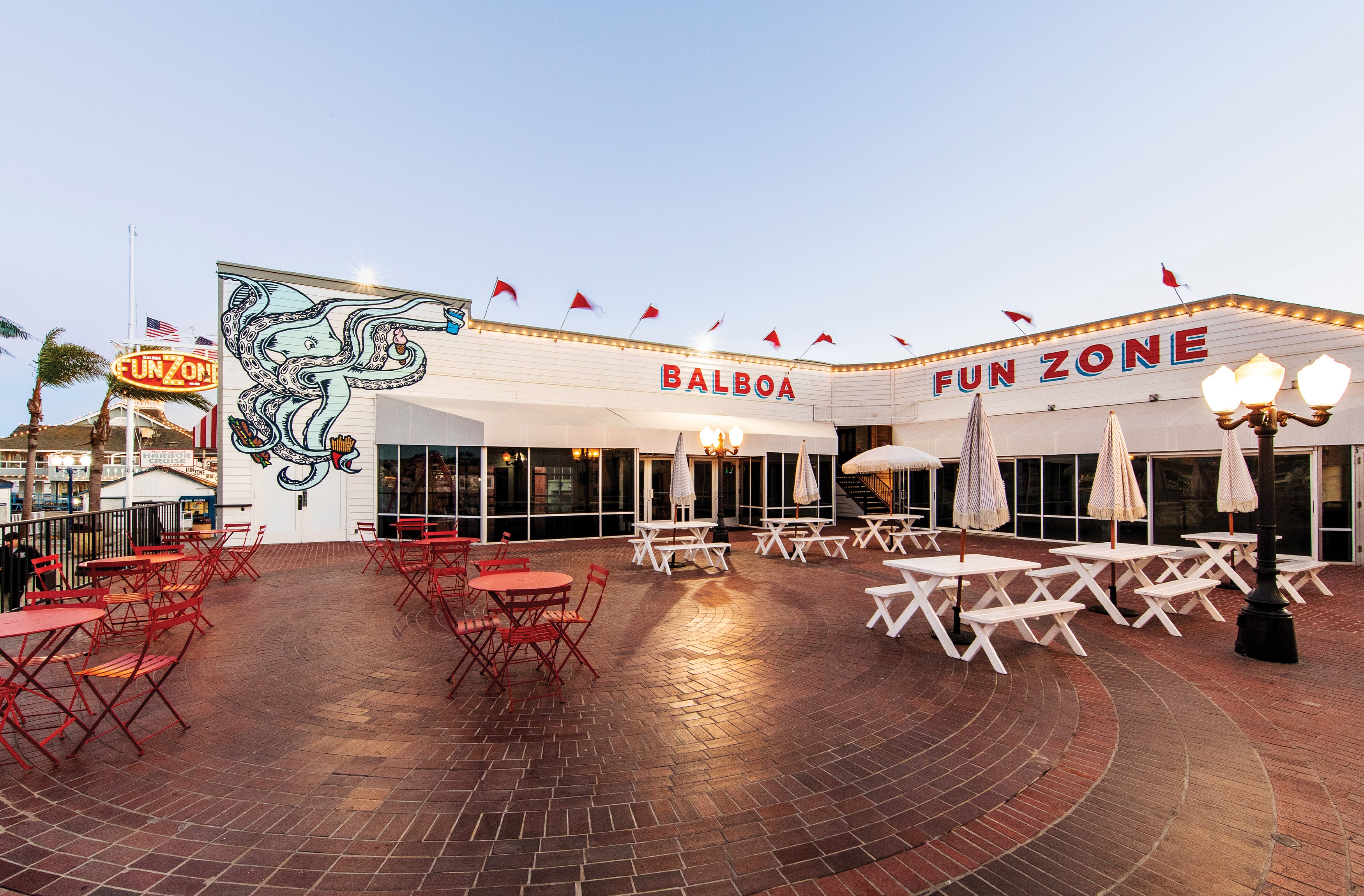 Image of the Balboa Fun Zone in Newport Beach, California with red lettered overhead signage and a playful octopus holding fries, ice cream and a shake. Painted mural of an octopus at the Balboa Fun Zone in Newport Beach, California.