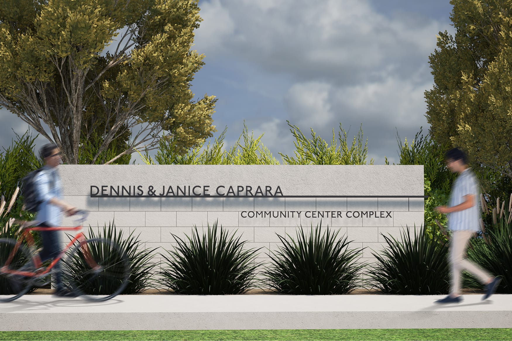 Rendering of a stone monument wall reading 'Dennis & Janice Caprara Community Center Complex,' framed by tall ornamental grasses and trees, with two blurred people walking and biking past on the sidewalk.