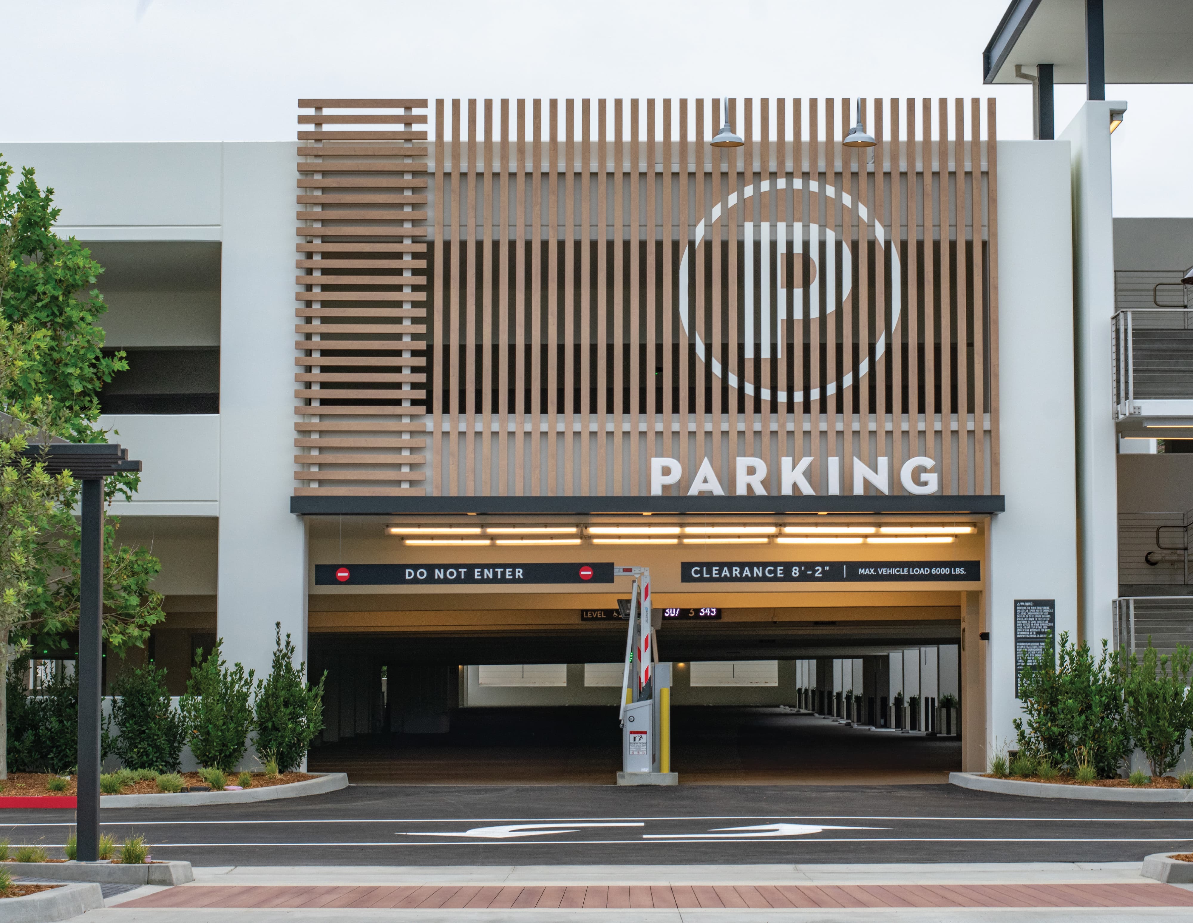 Dana Point Harbor parking garage entrance facade featuring a large-scale branded parking identification graphic with circular "P" symbol and dimensional "Parking" lettering on a warm wood slat screen panel, with vehicular clearance and regulatory signage at the entry gate — RSM Design wayfinding and signage design, master sign programs, specialty graphics, environmental graphic design, and branded environments for waterfront, parking garage, civic, and mixed-use destinations.
