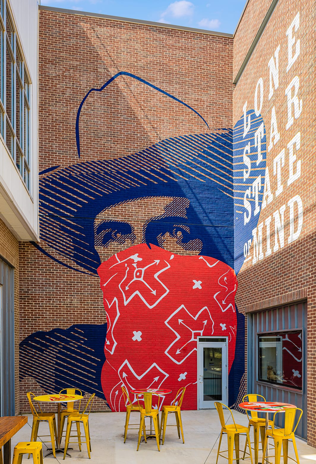 Large-scale exterior brick building mural of a cowboy figure with bold typography reading "Lone Star State of Mind" at Toyota Music Factory mixed-use entertainment district in Irving, Texas — RSM Design public art, murals, experiential graphics, and placemaking for mixed-use, food and beverage, and streetscape destinations.