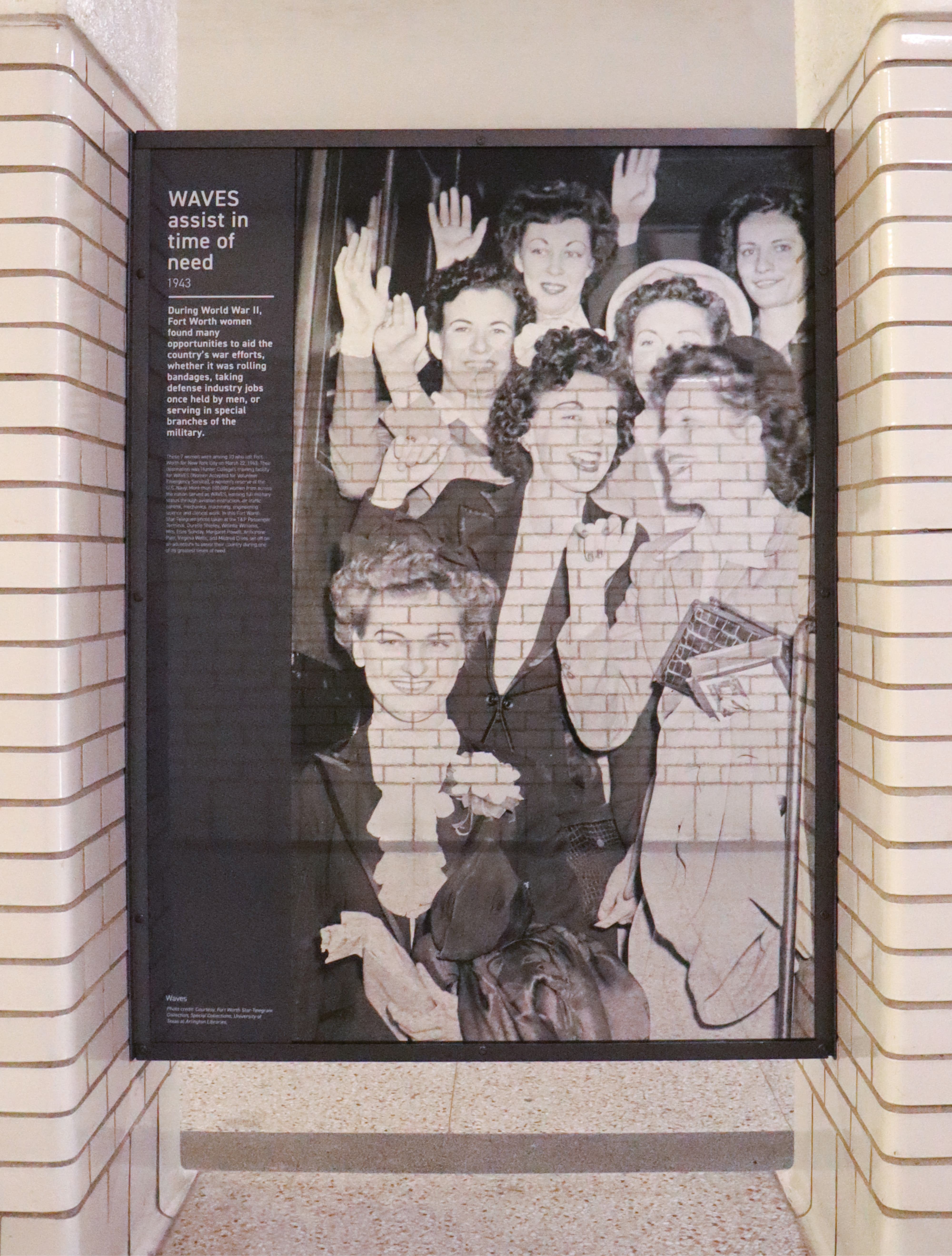 Historic interpretive exhibit panel titled "WAVES Assist in Time of Need, 1943" featuring a large-scale archival photograph of Fort Worth women waving goodbye at T&P Station during World War II, showcasing experiential graphics and cultural placemaking design for a mixed-use transit development by RSM Design.