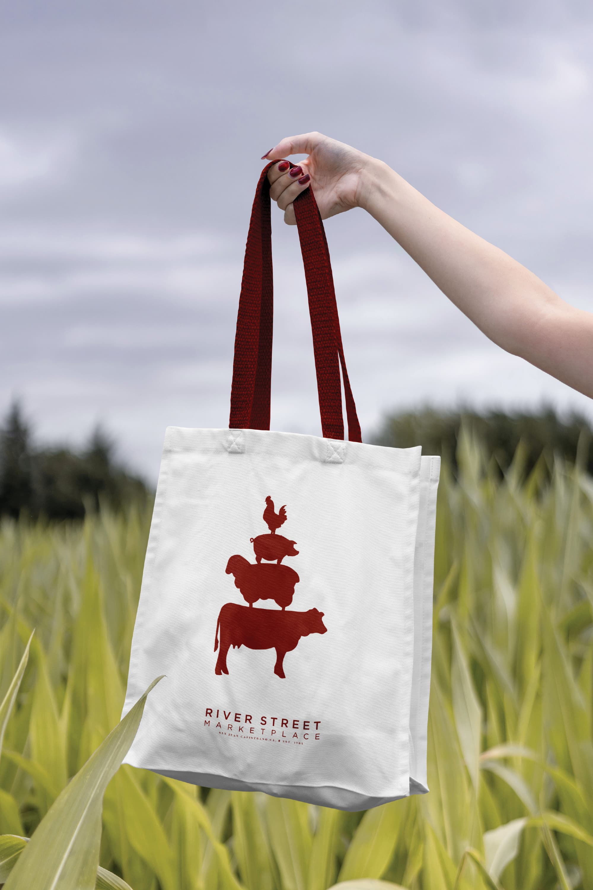 RSM Design branded tote bag for River Street Marketplace featuring a stacked farm animal silhouette logo in deep red on a white canvas bag, showcasing print and digital collateral design, visual identity, and placemaking branding for a food and beverage retail market environment.