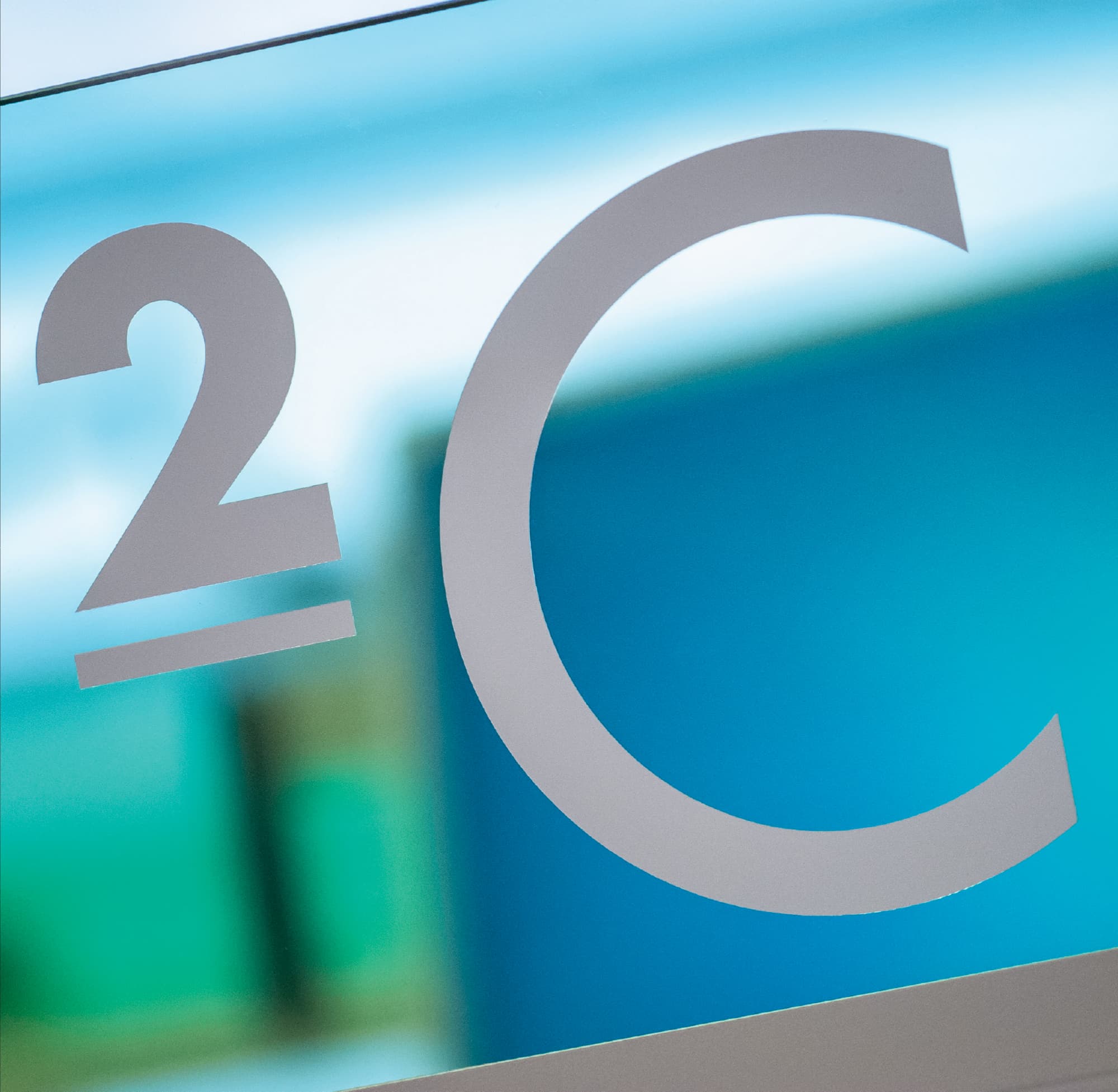 Close-up of a wayfinding sign reading "2C" with silver typography on frosted glass in a health and wellness facility, showcasing environmental graphic design and signage by RSM Design.