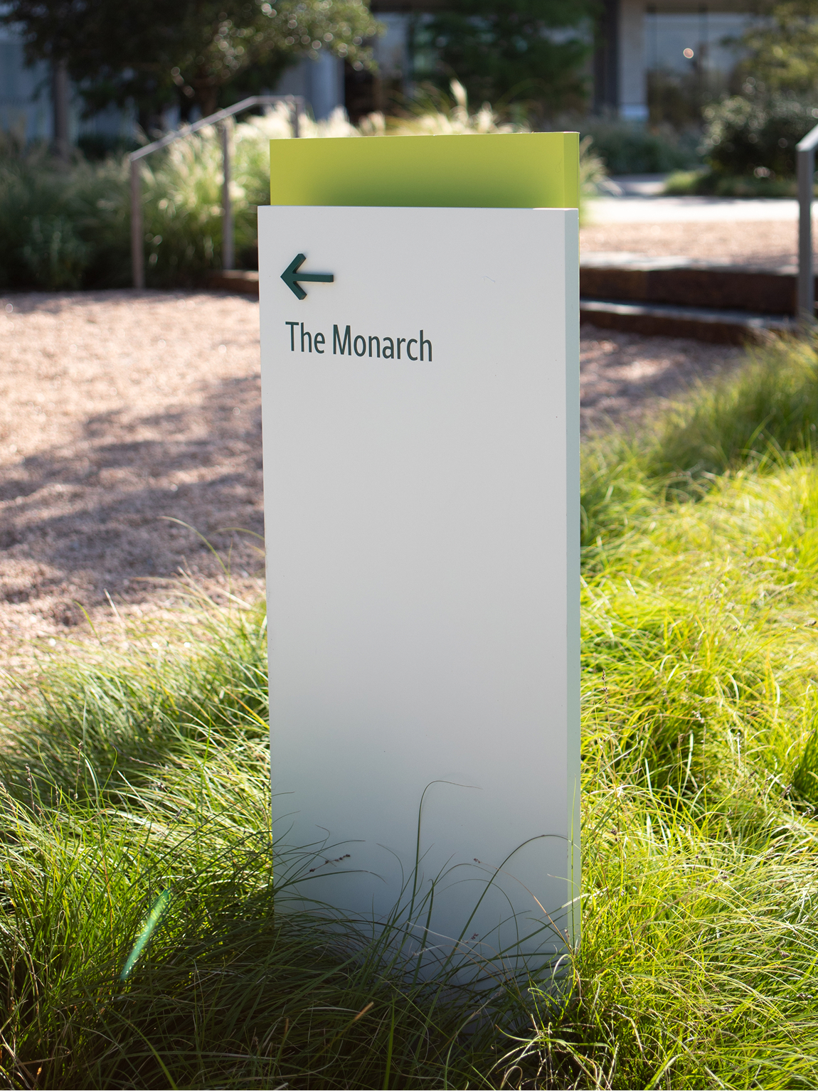 Kaleidoscope Park white and lime green directional wayfinding sign post pointing to The Monarch surrounded by lush ornamental grasses and native landscaping, Frisco, Texas