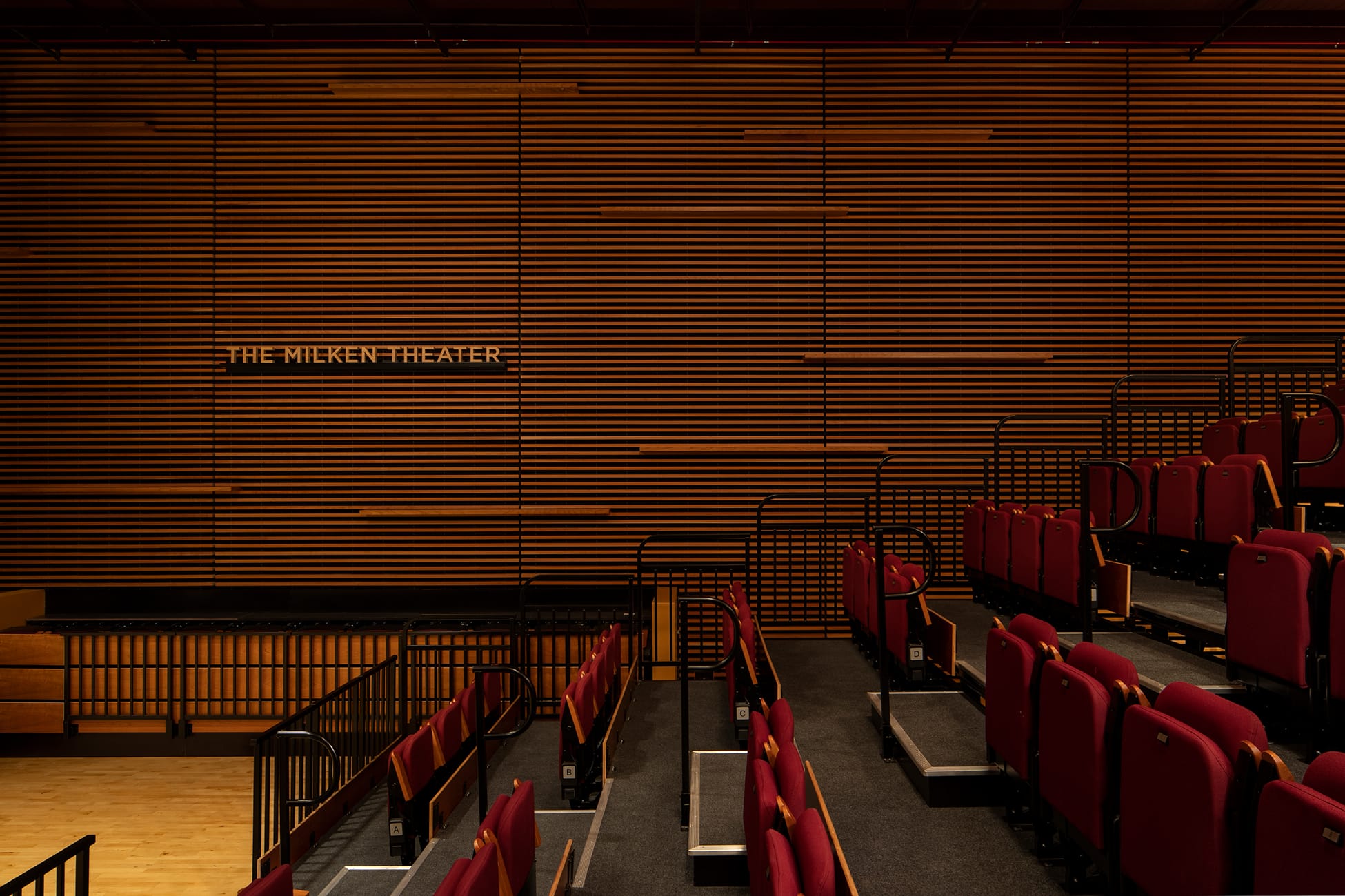 The Milken Theater identity signage on wood slat wall above red seating at Brentwood School campus in Los Angeles - donor recognition and environmental graphic design by RSM Design
