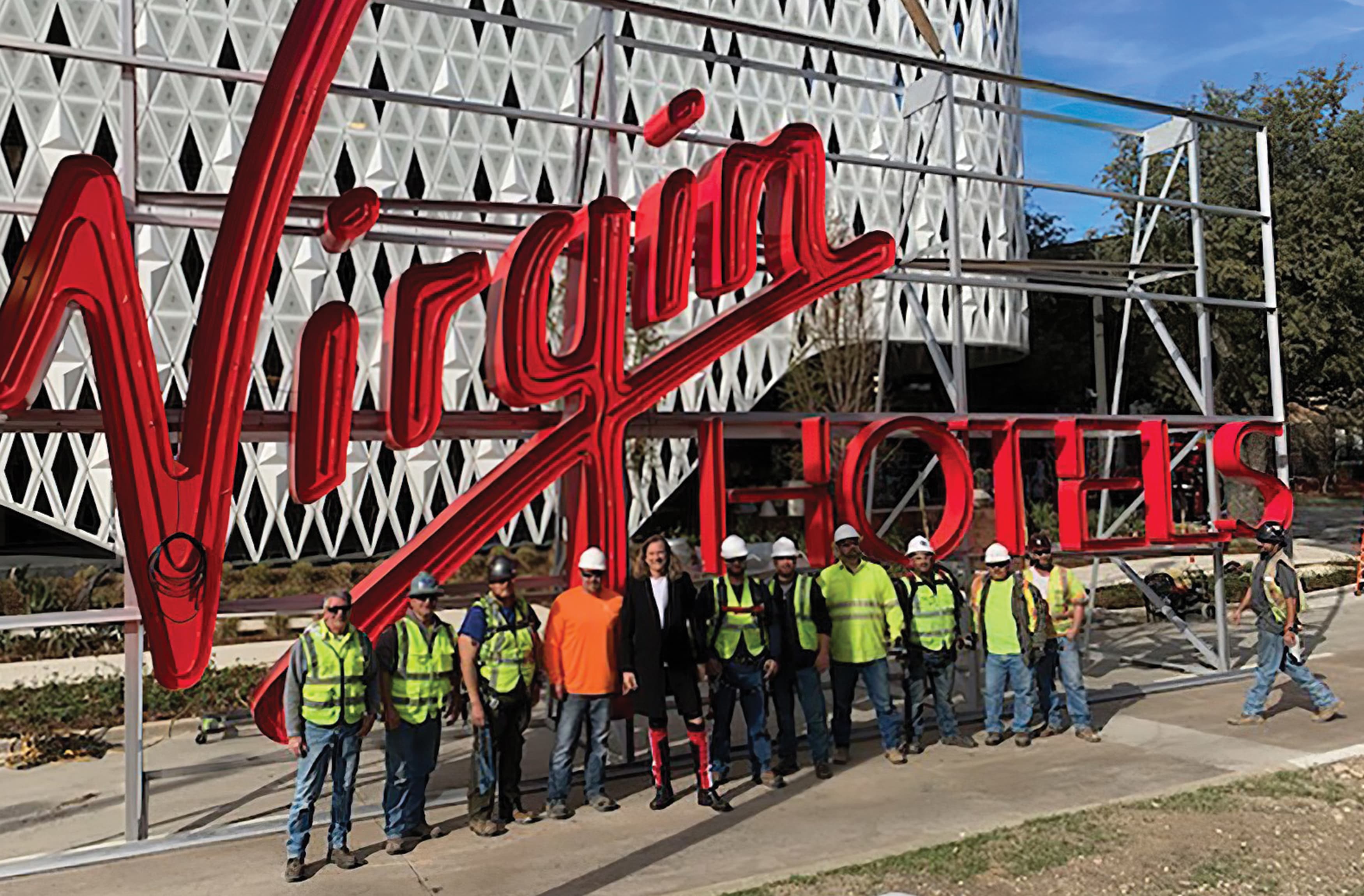 A photograph of a large fabricated sign for the new Virgin hotel featuring the installation team.