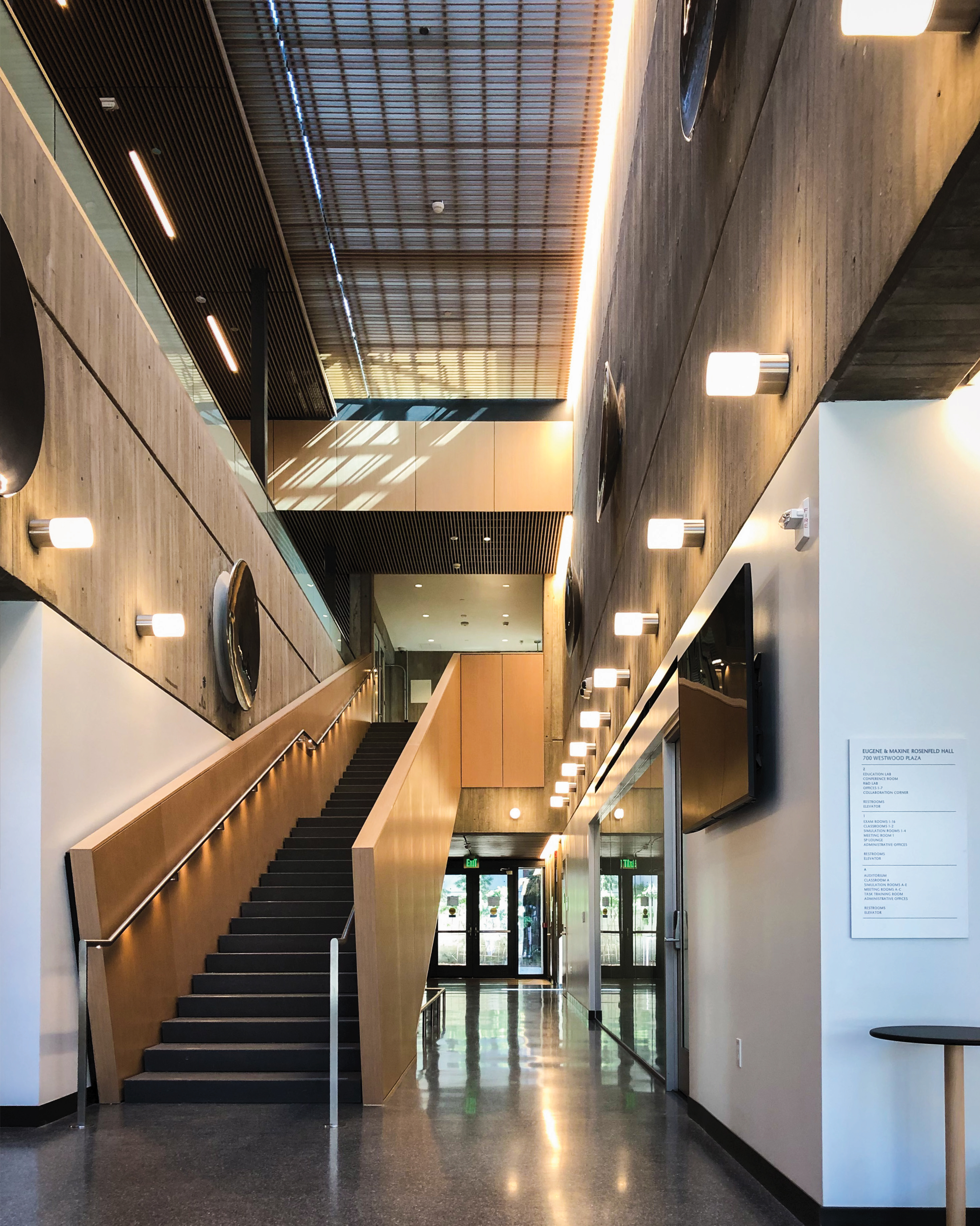 Interior architecture and environmental graphic design at Eugene & Maxine Rosenfeld Hall featuring integrated wayfinding signage, branded environments, and experiential design for a higher education campus facility.