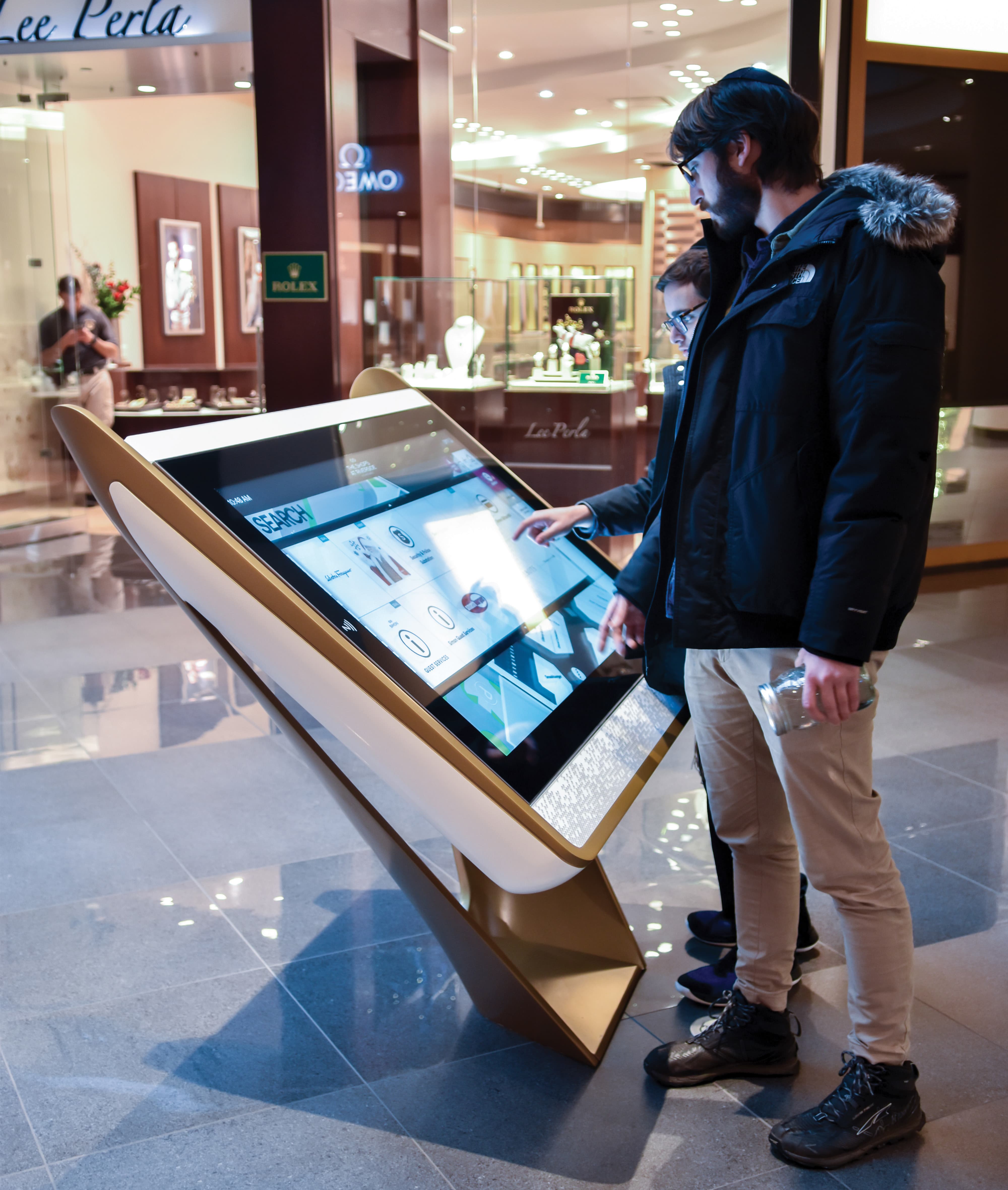 Visitors using an interactive digital directory in a retail mall, showcasing environmental graphic design, wayfinding systems, and experiential design that enhance navigation and customer experience in mixed-use retail and shopping destinations.
