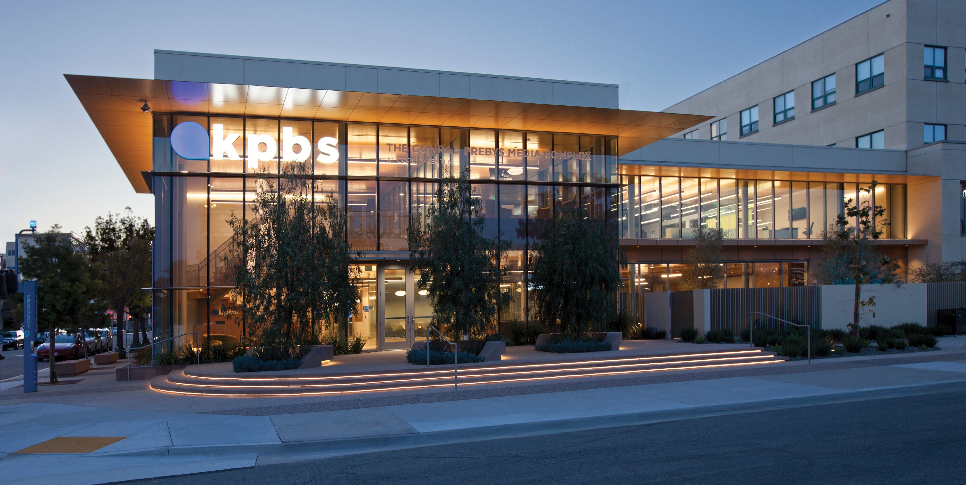 Exterior view of KPBS Conrad Prebys Media Complex at dusk featuring illuminated architectural signage, integrated branding, and site wayfinding, reflecting RSM Design expertise in environmental graphic design for media, corporate, and civic environments.