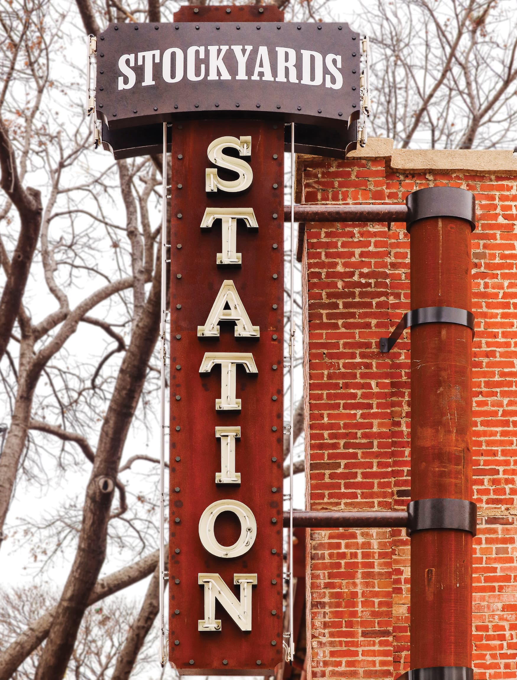 Close up of the Stockyards Station vertical marquee sign with outlined letters in a rustic style against a brick wall. 