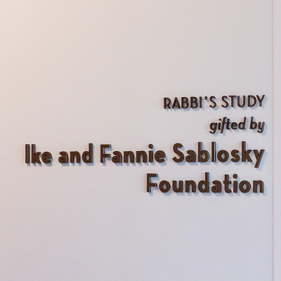 Wall sign reading 'Rabbi's Study, gifted by Ike and Fannie Sablosky Foundation' in brown dimensional lettering on a white wall.