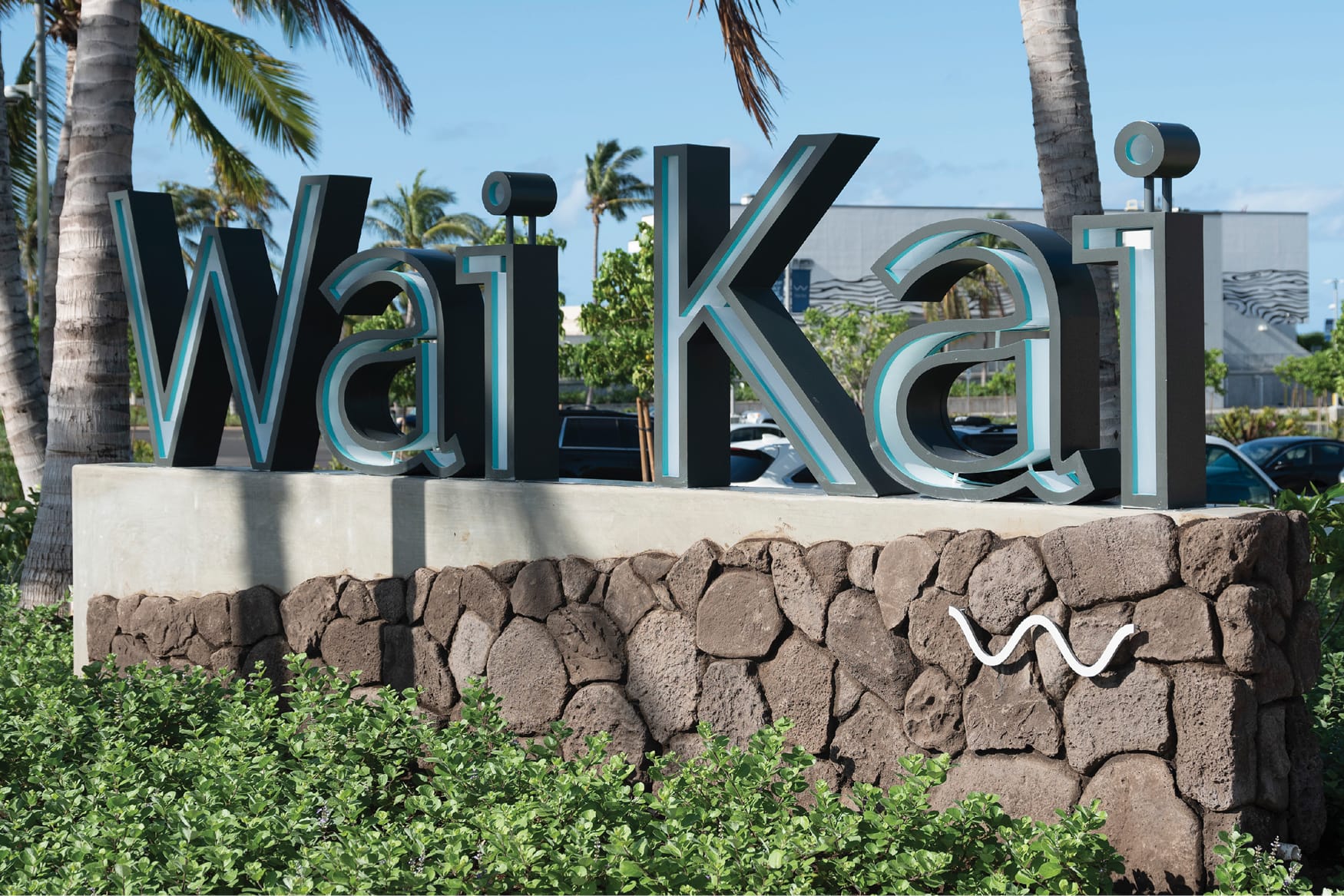 Dimensional Wai Kai monument sign with wave symbol on lava rock base framed by palm trees, Ewa Beach, Oahu, environmental graphic design by RSM Design.