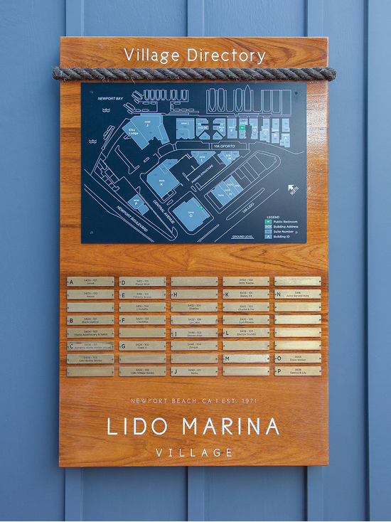 Lido Marina Village directory board with nautical rope detail, site map, and brass tenant listing plaques mounted on warm wood panel against blue wall in Newport Beach, California