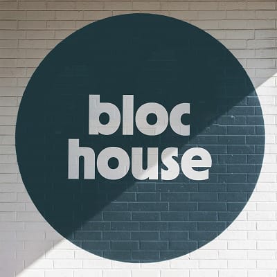 The "bloc house" wordmark painted as a large dark teal circle mural on a white brick wall, with the name in bold white type centered within the circle.