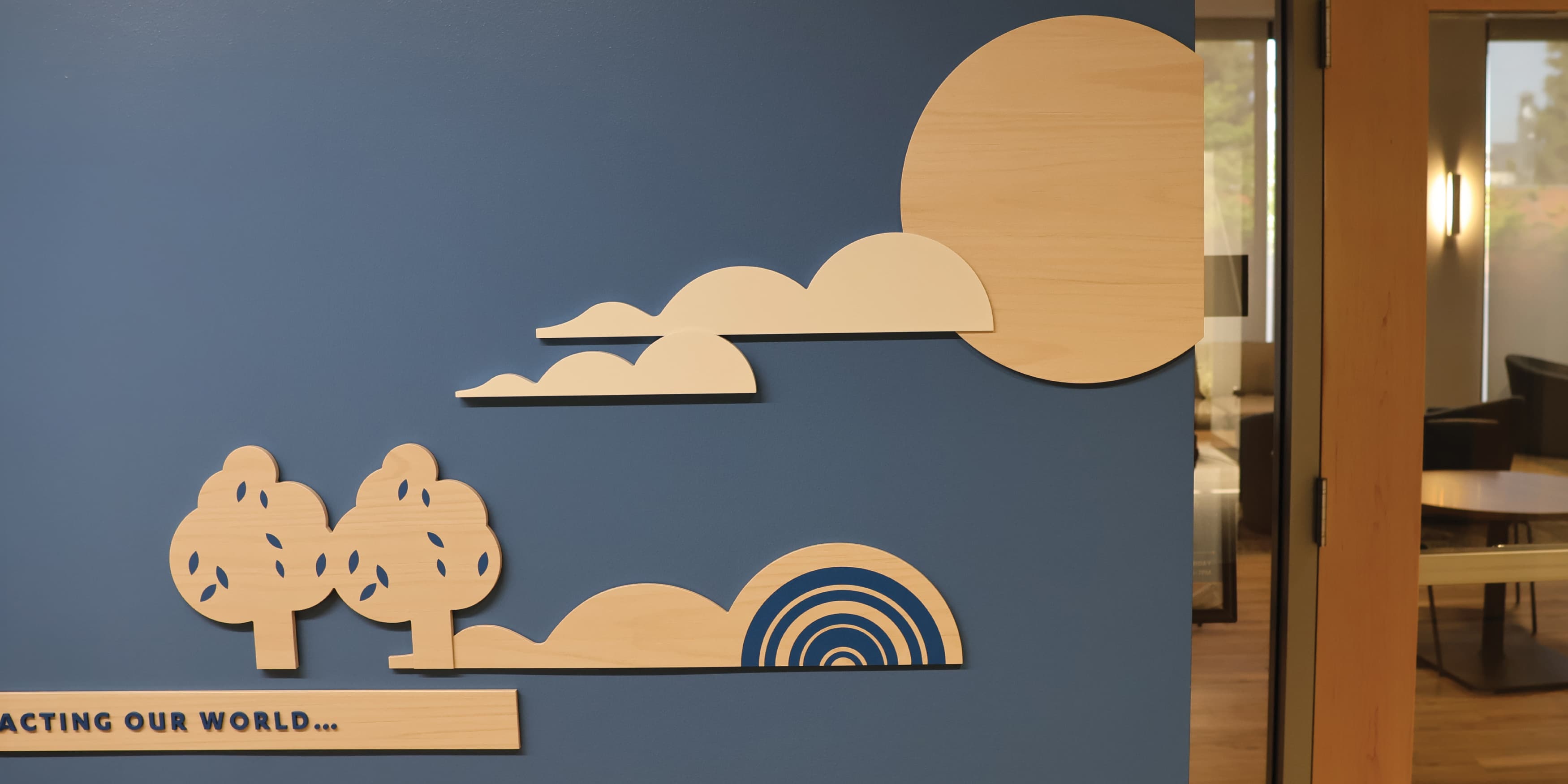The wall in the image is part of the permanent exhibition designed by RSM Design for the UCLA Fielding School of Public Health's 60th anniversary. It features a vibrant and informative display with a variety of graphic elements and icons. Key public health themes such as Inclusion, Equity, Evidence, Prevention, Community, and Impact are highlighted on the wall, each with its own distinct section. The design includes detailed illustrations, representing different aspects of public health and the school's contributions to the field. The wall is well-lit and incorporates wooden textures with colorful visual elements, making the information engaging and accessible. There are also seating benches integrated into the design, inviting viewers to spend time interacting with the exhibit.