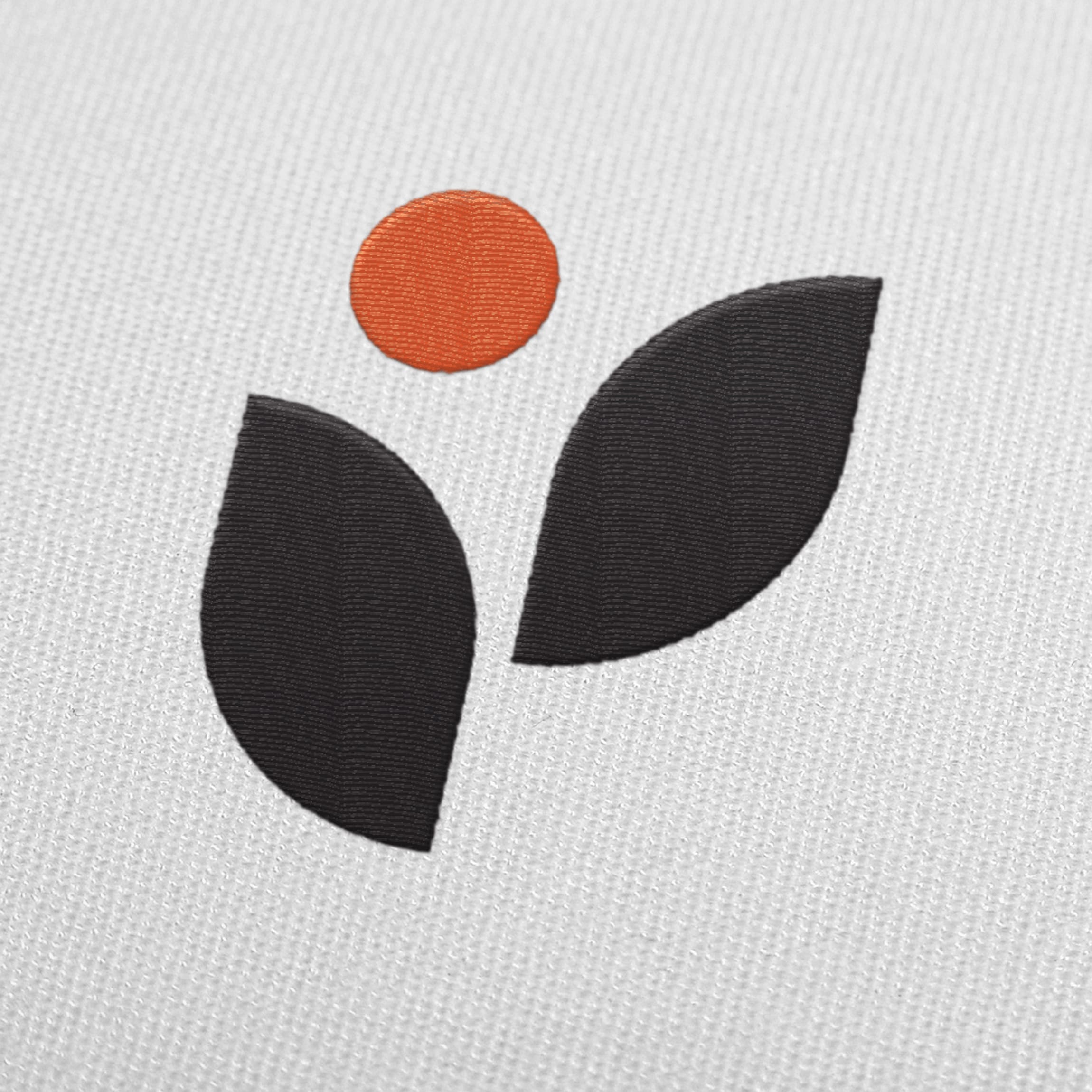 Close-up of an embroidered leaf-and-dot icon in black and orange thread on white fabric — brand identity mockup by RSM Design.