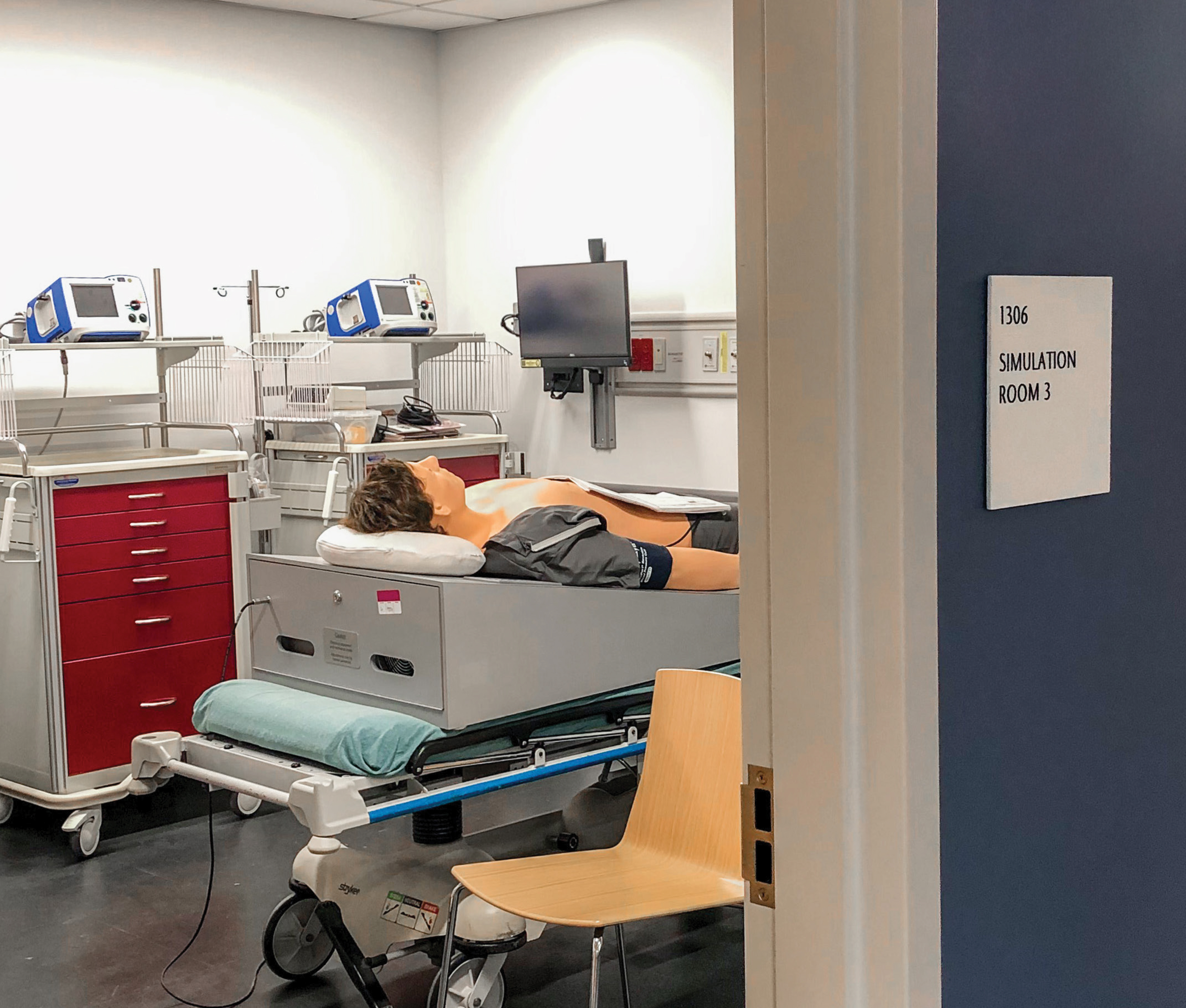 Healthcare simulation lab within a university campus facility featuring medical training equipment and integrated environmental graphic design and wayfinding signage supporting healthcare and higher education environments.