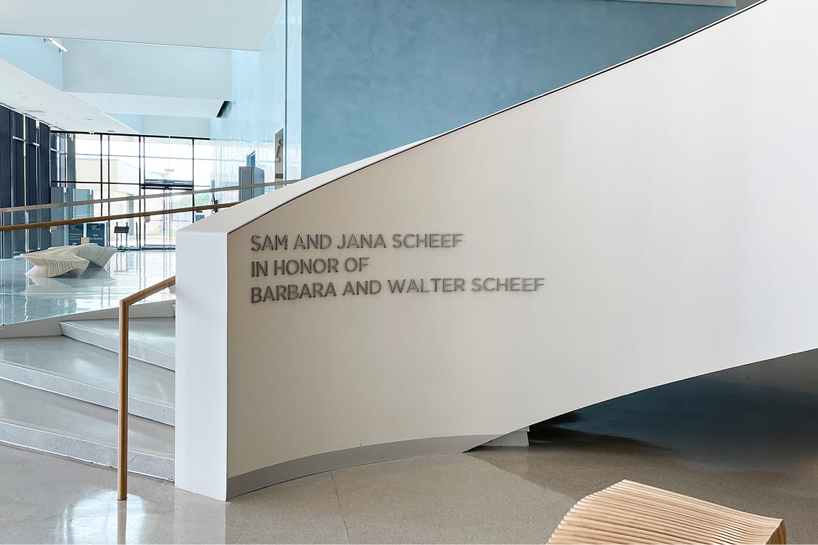 Donor recognition lettering reading 'Sam and Jana Scheef in Honor of Barbara and Walter Scheef' on a curved white staircase wall in the light-filled lobby of Buddy Holly Hall of Performing Arts and Sciences, Lubbock Texas