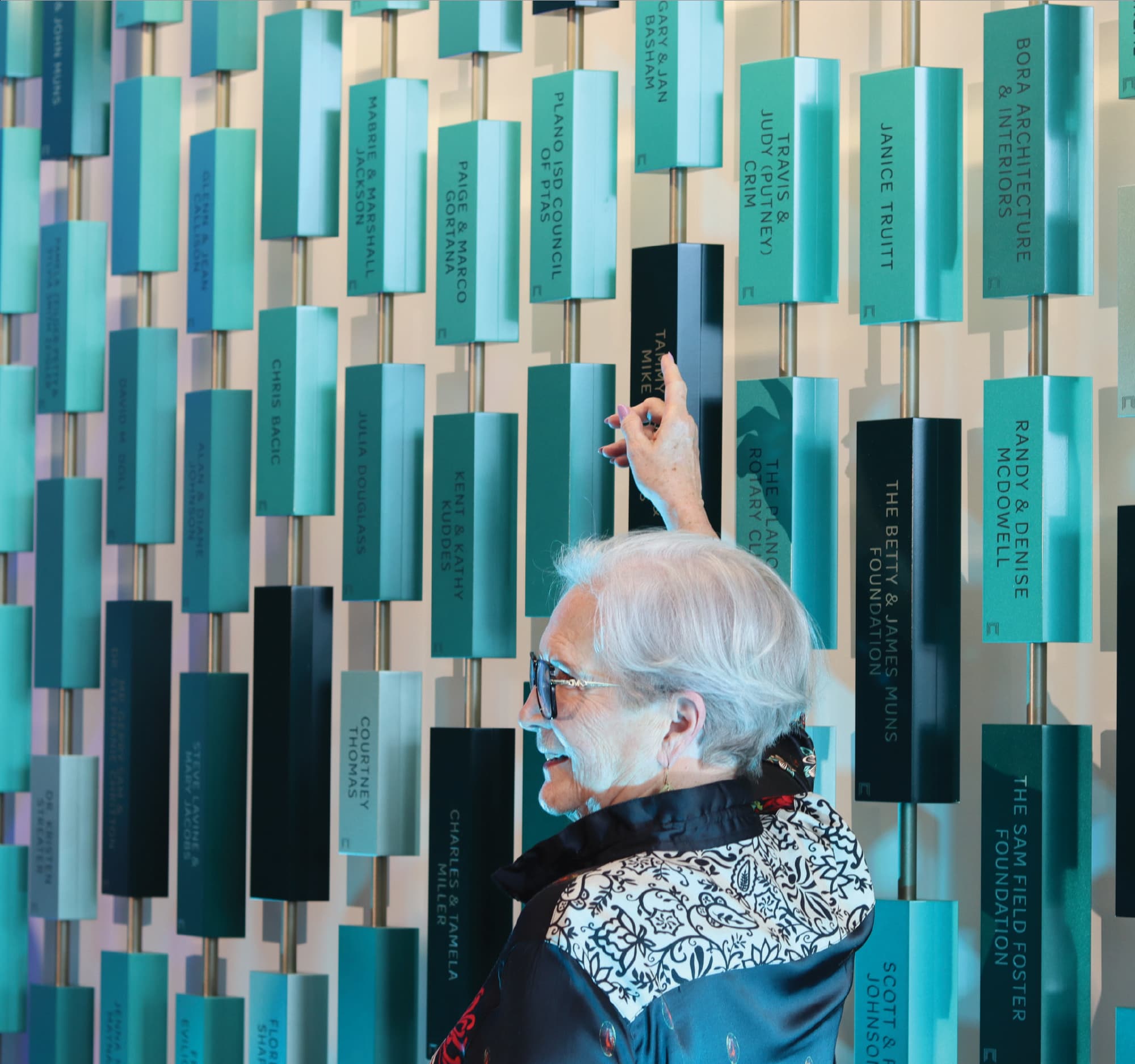 Visitor interacting with a dimensional donor recognition wall featuring engraved donor plaques, highlighting environmental graphic design, experiential storytelling, and placemaking within higher education and healthcare environments.