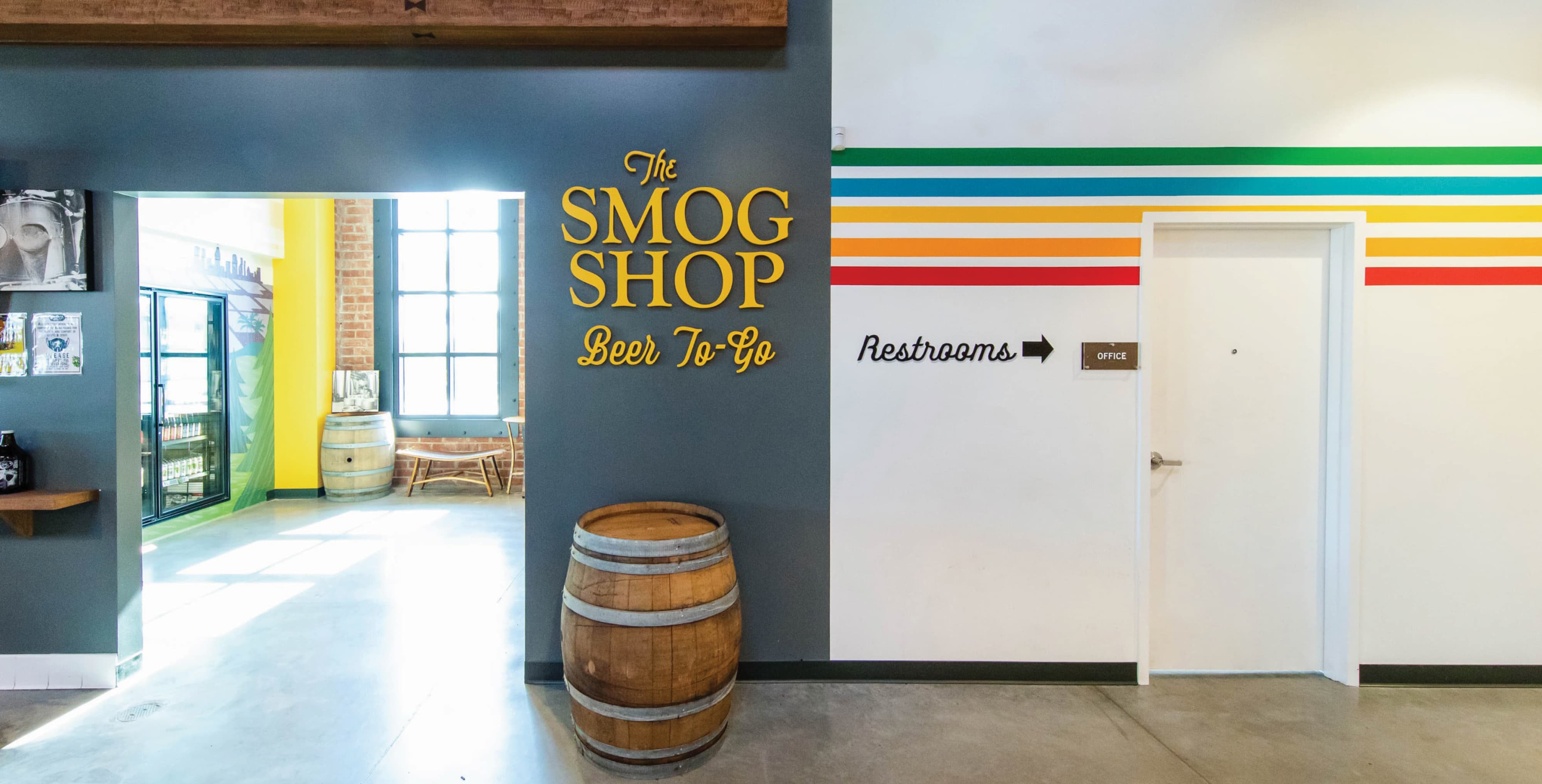 Interior environmental graphic design and wayfinding system featuring branded “The Smog Shop Beer To-Go” signage and restroom directional graphics, integrating brand identity, placemaking, and signage design for a retail and hospitality destination by RSM Design