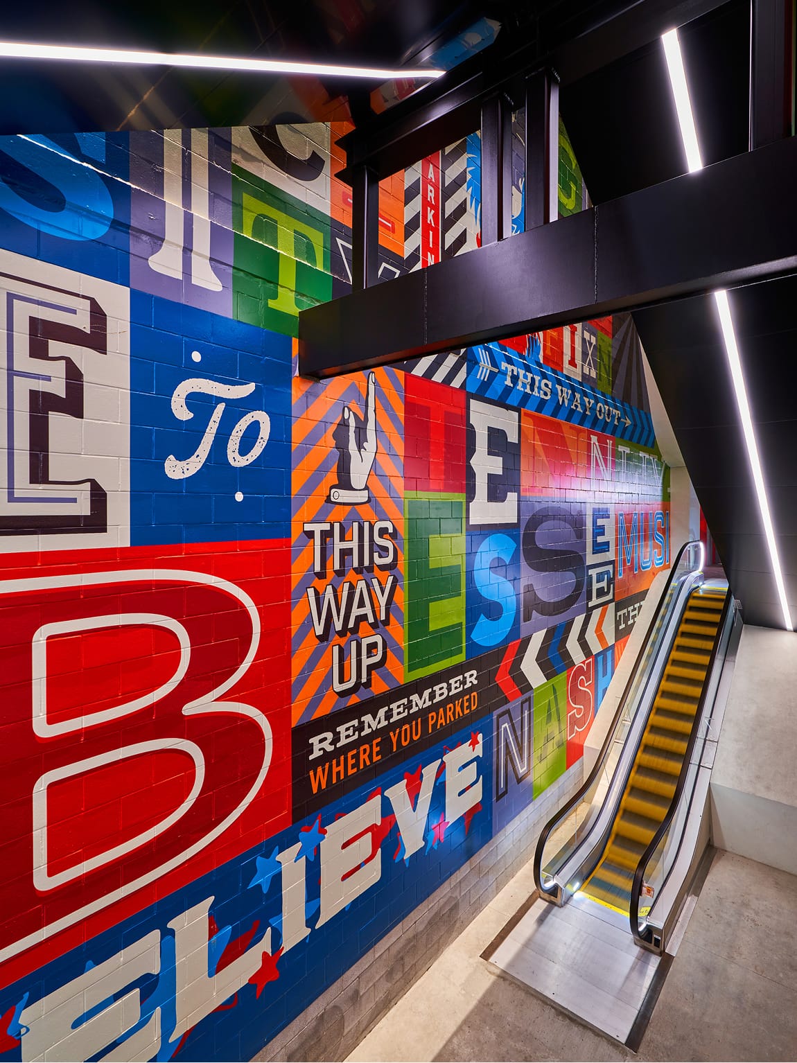 Escalator corridor at Fifth + Broadway featuring a large-scale graphic mural that combines bold typography and directional messaging to enhance wayfinding and reinforce the district’s identity.