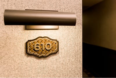 Hotel Drover guest room number 610 featuring an ornate brass door plate with Western-style tooled leather pattern detailing and a modern wall sconce above