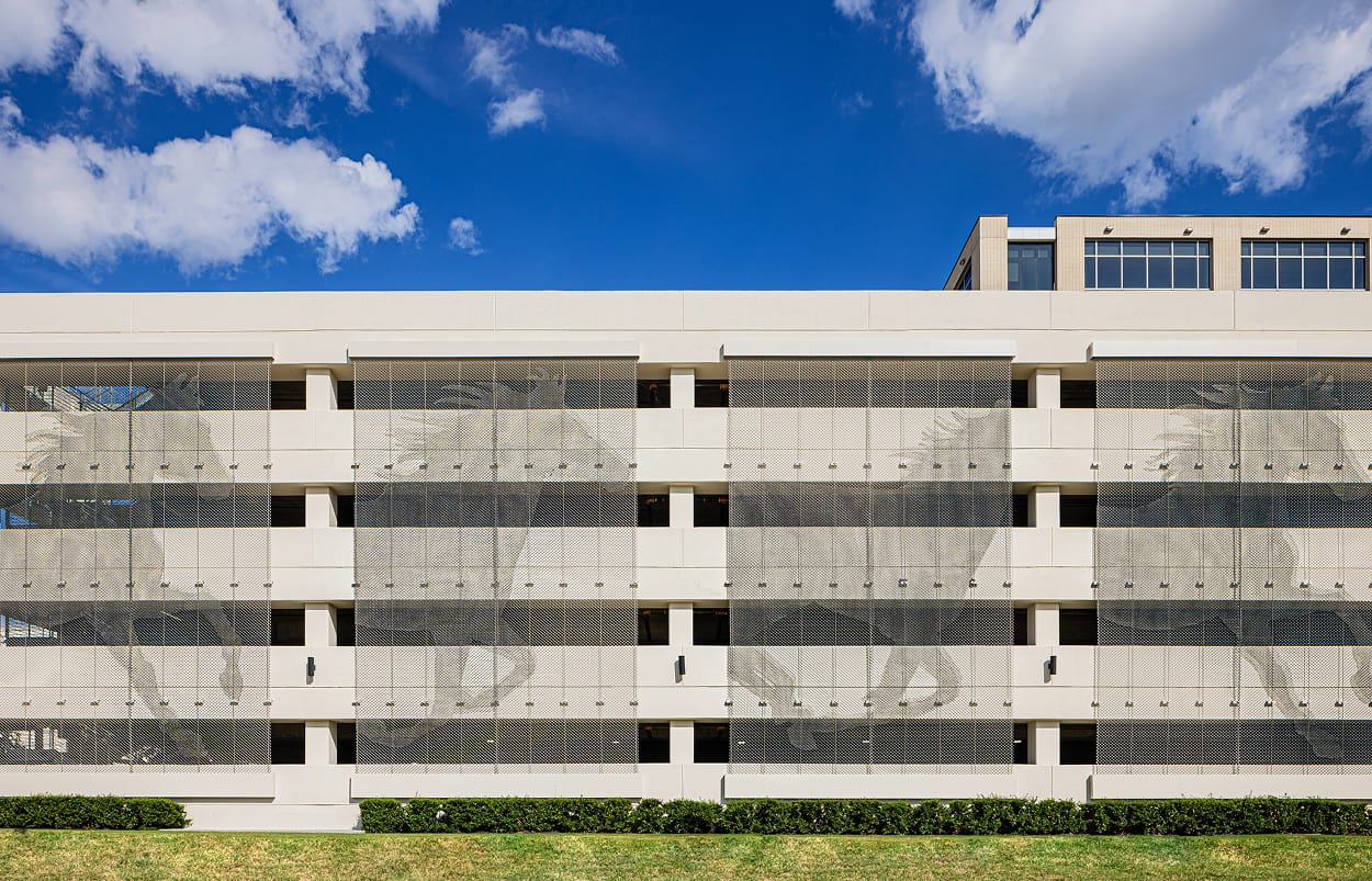 Multi-story parking garage exterior facade with large-scale perforated metal screen panels featuring botanical and figural experiential graphics spanning multiple levels — RSM Design specialty graphics, experiential graphics, branded environments, and placemaking for parking garage and mixed-use destinations.