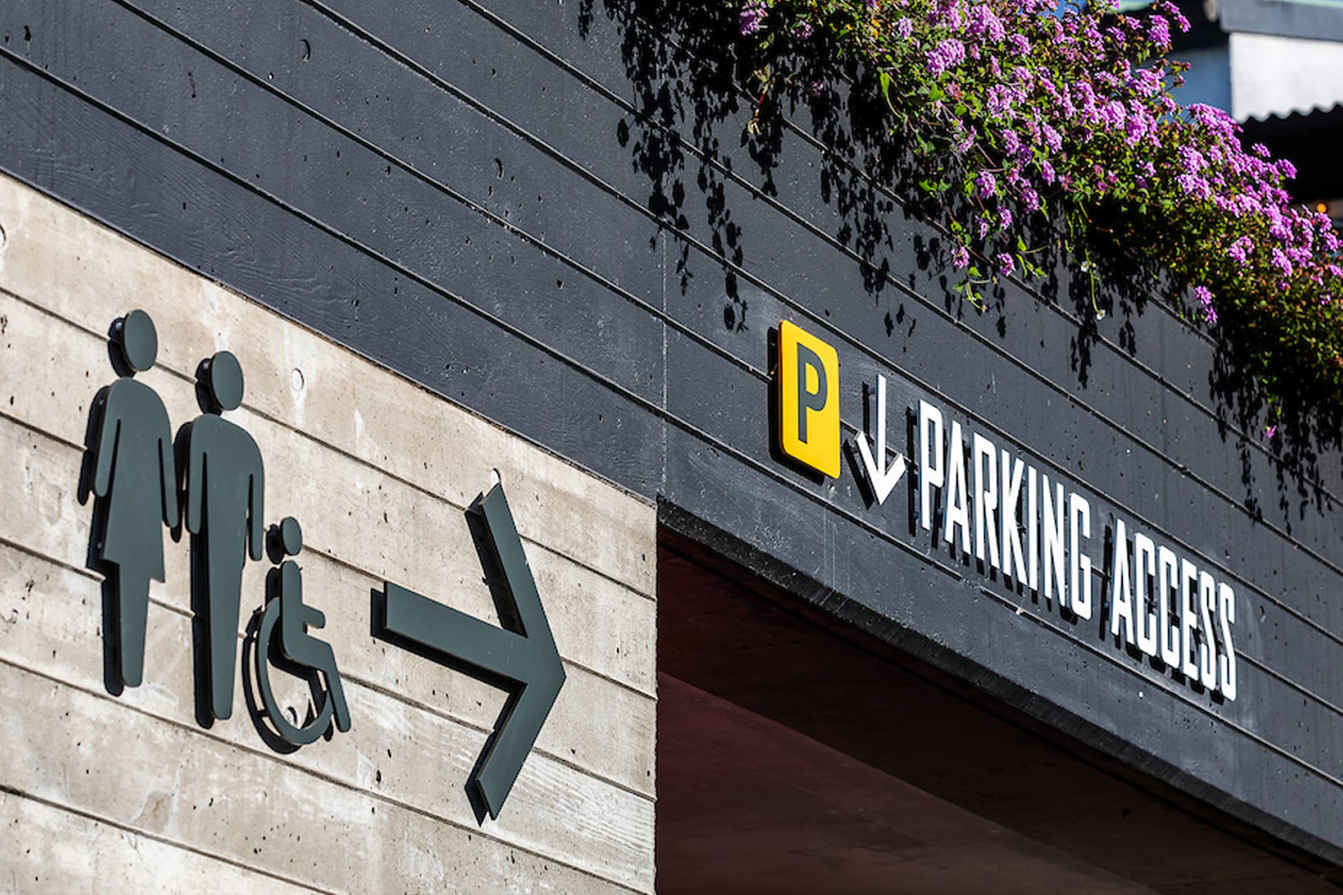 Jack London Square exterior signage showing ADA-accessible restroom directional sign with wheelchair symbol and yellow parking access sign with arrow, Oakland, California