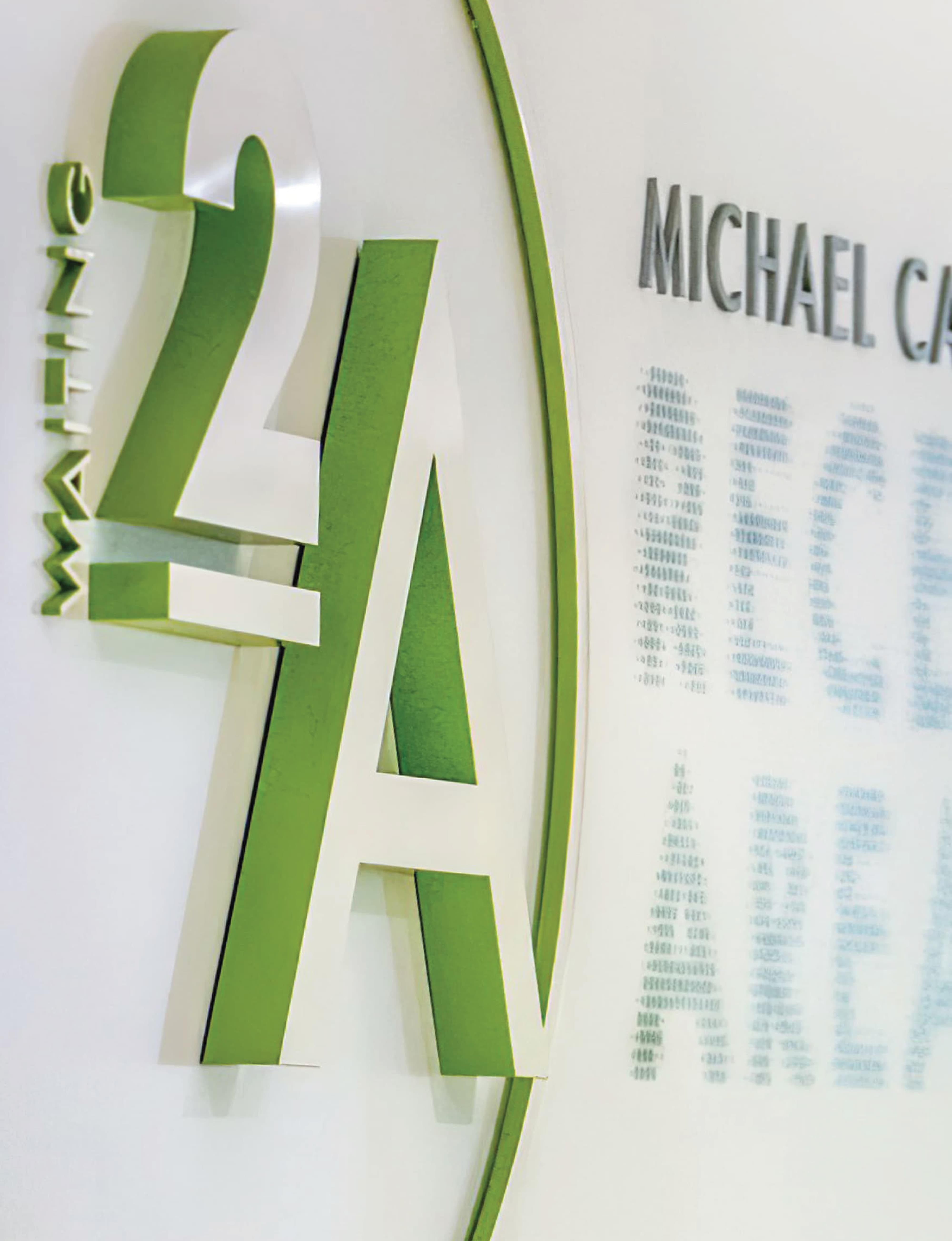 Close-up detail of a dimensional green "2A" room identification sign with layered letterforms and circular arc element alongside a printed donor name list panel and "Michael Ca—" named space recognition at University of the Pacific Arthur A. Dugoni School of Dentistry in San Francisco — RSM Design donor recognition and specialty graphics, wayfinding and signage design, branded environments, and environmental graphic design for education and health and wellness destinations.