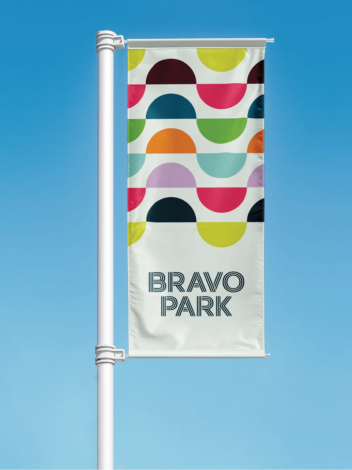 RSM Design Bravo Park — branded lamppost banner with multicolour geometric pattern and Bravo Park logo against a blue sky, park wayfinding and placemaking signage design