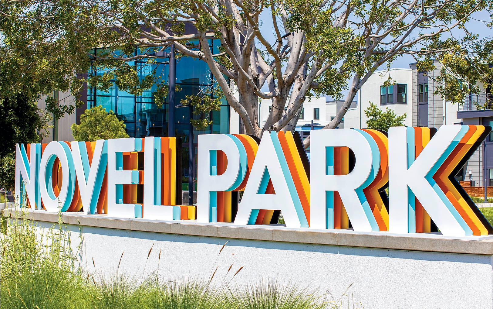 Bold three-dimensional "Novel Park" monument sign with layered white, orange, yellow, and teal letters installed at the Novel Park neighborhood entrance in Irvine, California, designed by RSM Design
