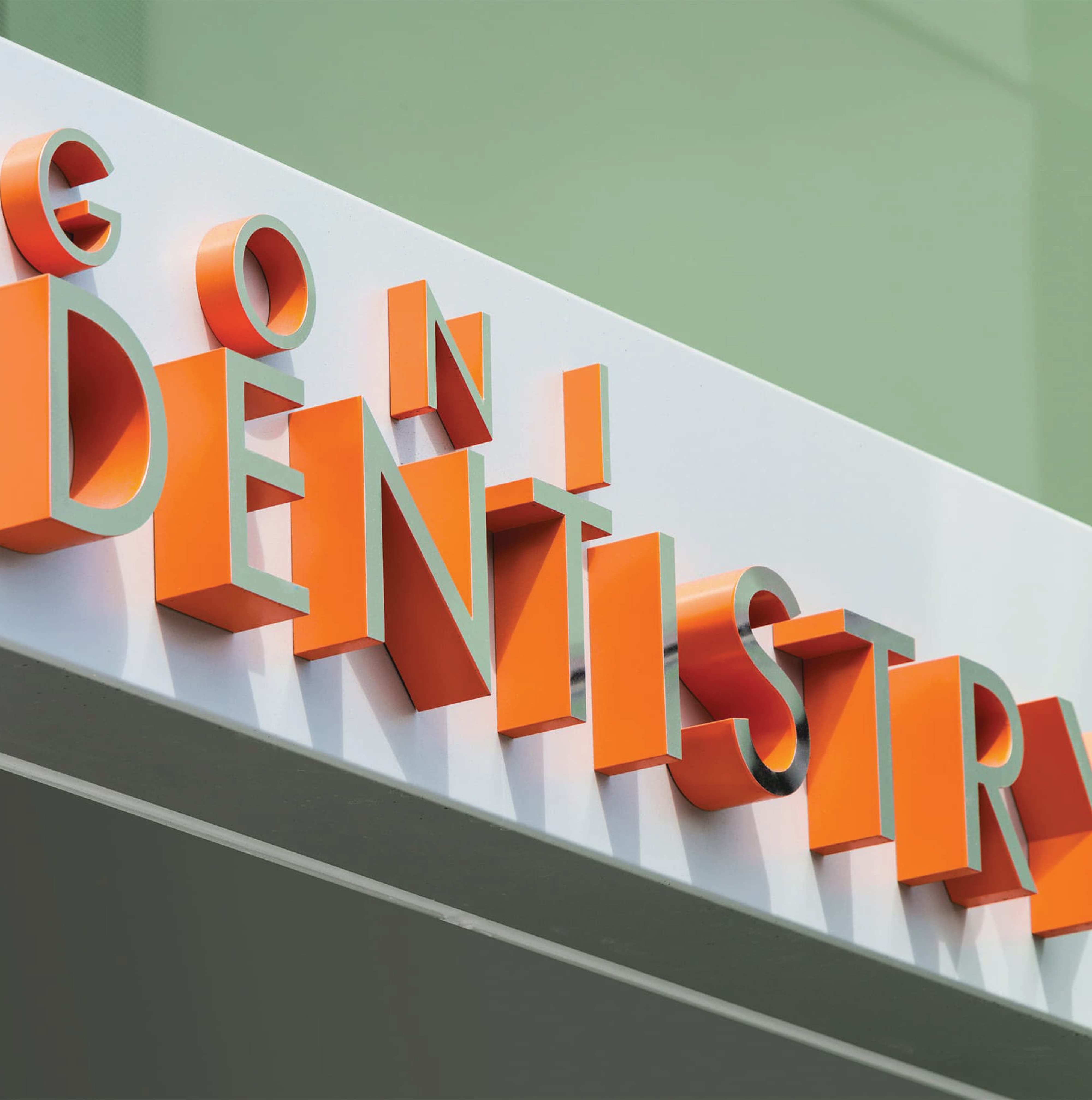 Close-up detail of bold orange dimensional "Dugoni Dentistry" exterior building identification letterforms with brushed metal returns mounted on a white fascia panel at University of the Pacific Arthur A. Dugoni School of Dentistry in San Francisco — RSM Design branding and visual identity, wayfinding and signage design, specialty graphics, and environmental graphic design for education and health and wellness destinations.