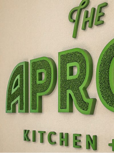 Close-up of The Approach Kitchen dimensional wall signage featuring bold green letters with textured grass-like face and raised green returns at Omni PGA Frisco