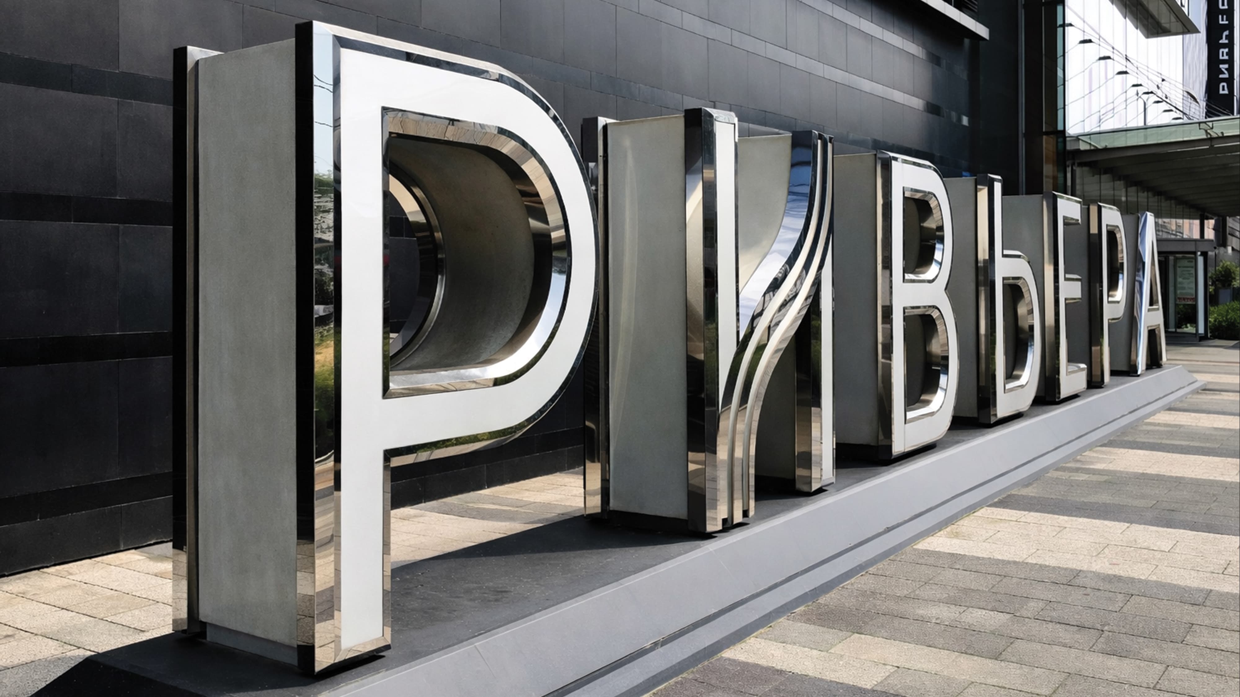 Large-scale polished stainless steel dimensional Cyrillic letterform landmark sign for Riviera international retail and mixed-use destination at a building entrance plaza — RSM Design specialty graphics, branding and visual identity, wayfinding and signage design, and experiential placemaking for retail, mixed-use, streetscape, and international destinations.