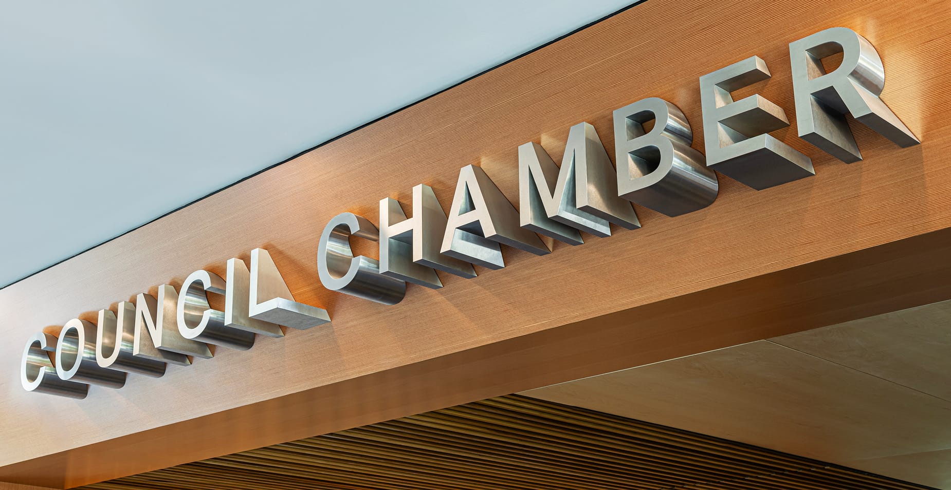 Close-up of Council Chamber large-scale brushed stainless steel dimensional letters mounted on warm wood panel fascia at Fort Worth City Hall
