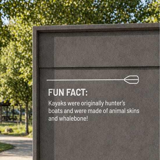Dark interpretive sign at Grand Park with a kayak paddle icon reading "Fun Fact: Kayaks were originally hunter's boats and were made of animal skins and whalebone!"