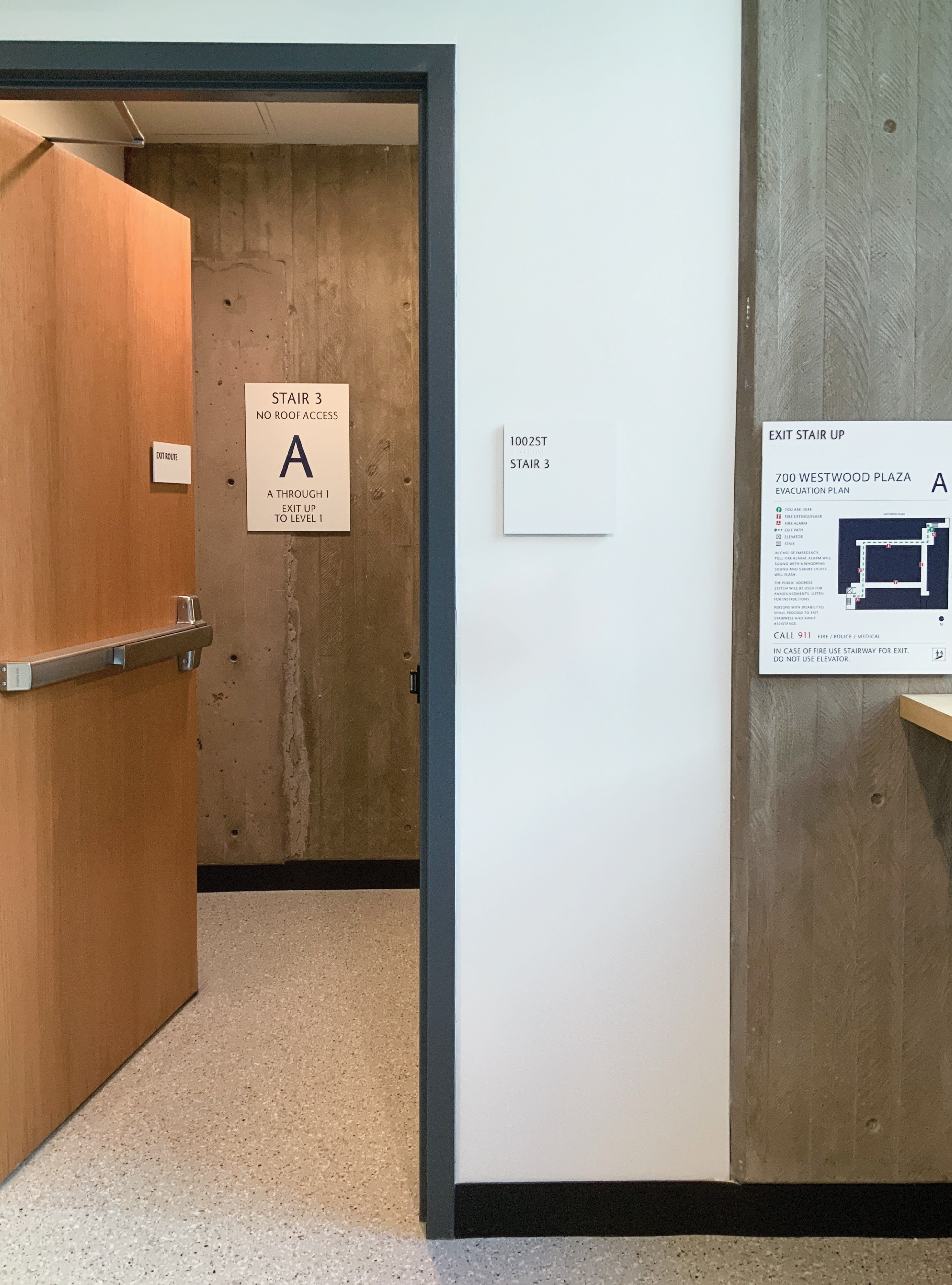 Interior environmental graphic design and life safety wayfinding signage directing to stairwell access and evacuation routes within a higher education campus building, illustrating integrated wayfinding systems and architectural signage.