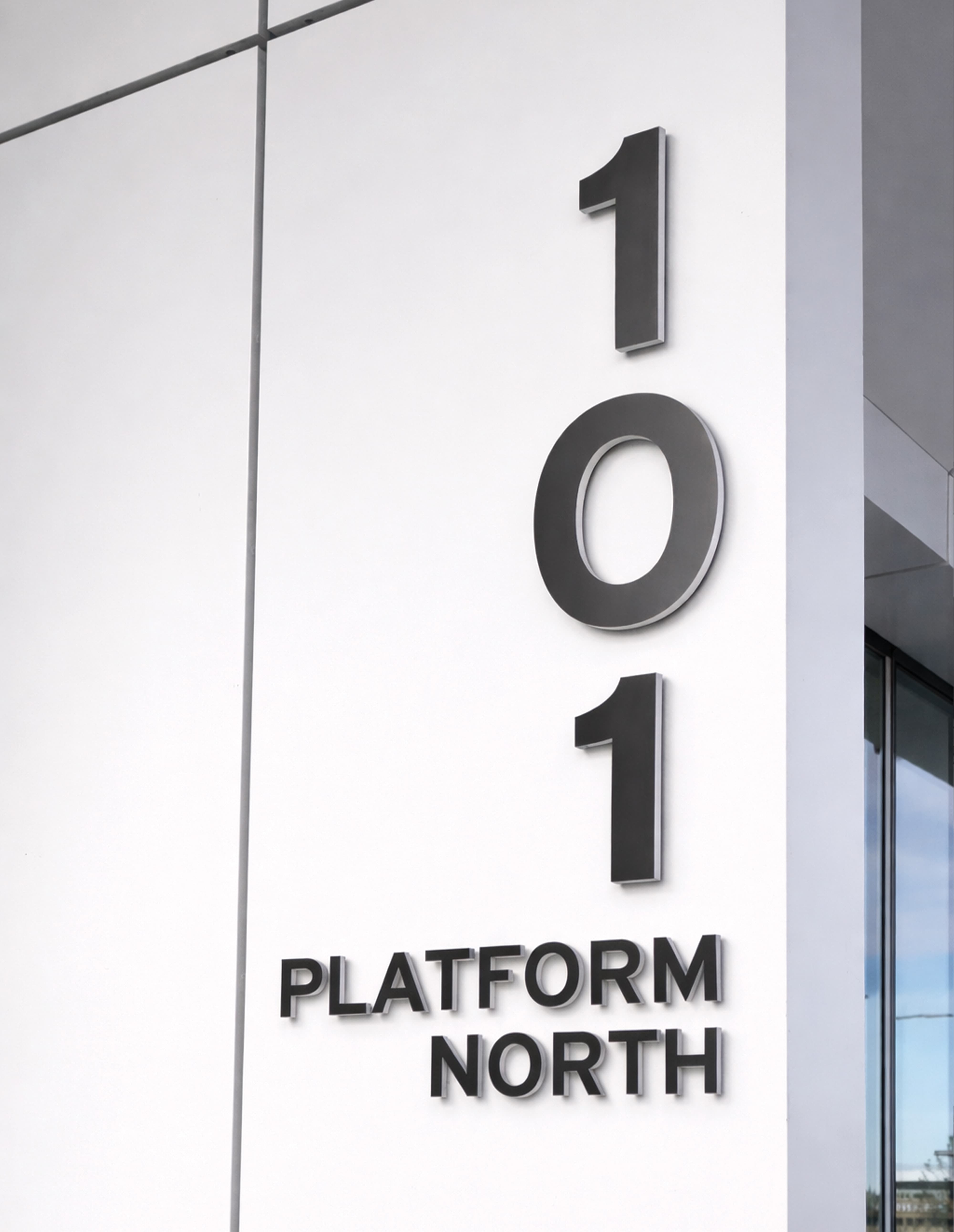 Dimensional black building identification signage reading "101 Platform North" mounted vertically on a white exterior facade, showcasing wayfinding and signage design for a mixed-use workplace environment by RSM Design.
