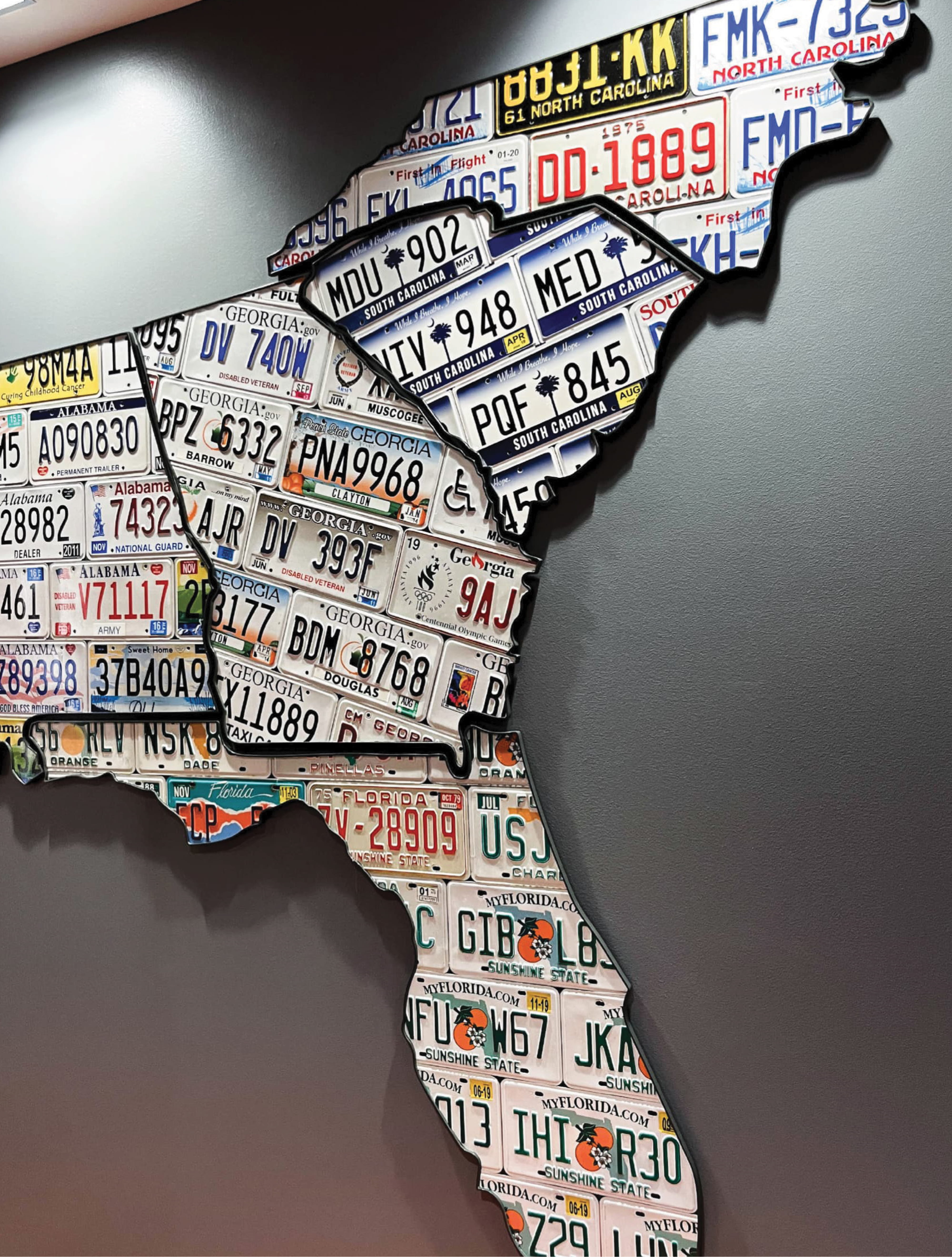 Custom environmental graphic design installation featuring a U.S. regional map composed of license plates, illustrating brand storytelling and placemaking through layered materials and experiential design within a corporate workplace environment.