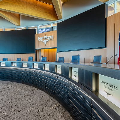 Fort Worth City Hall Council Chamber curved dais with individual council member nameplates featuring longhorn logo, Fort Worth dimensional sign on wood backdrop, large display screens, and wood lattice ceiling