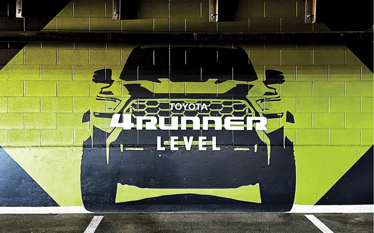 Toyota 4Runner branded level identification wall mural in bold yellow-green and black on a concrete block parking garage wall at Toyota Music Factory in Irving, Texas — RSM Design experiential graphics, branded environments, specialty graphics, and wayfinding and signage design for parking garage and mixed-use destinations.