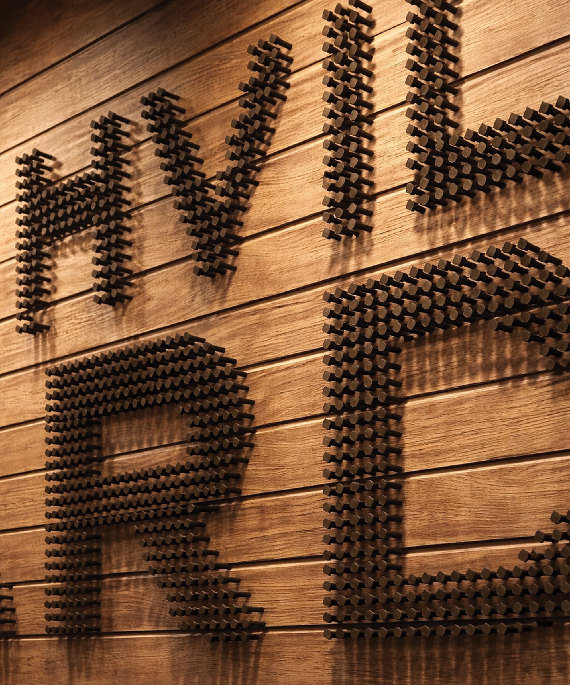 Close-up of dimensional nail-head lettering casting dramatic shadows on a warm wood plank wall, showcasing specialty graphics and experiential graphic design craftsmanship for a mixed-use workplace environment by RSM Design.
