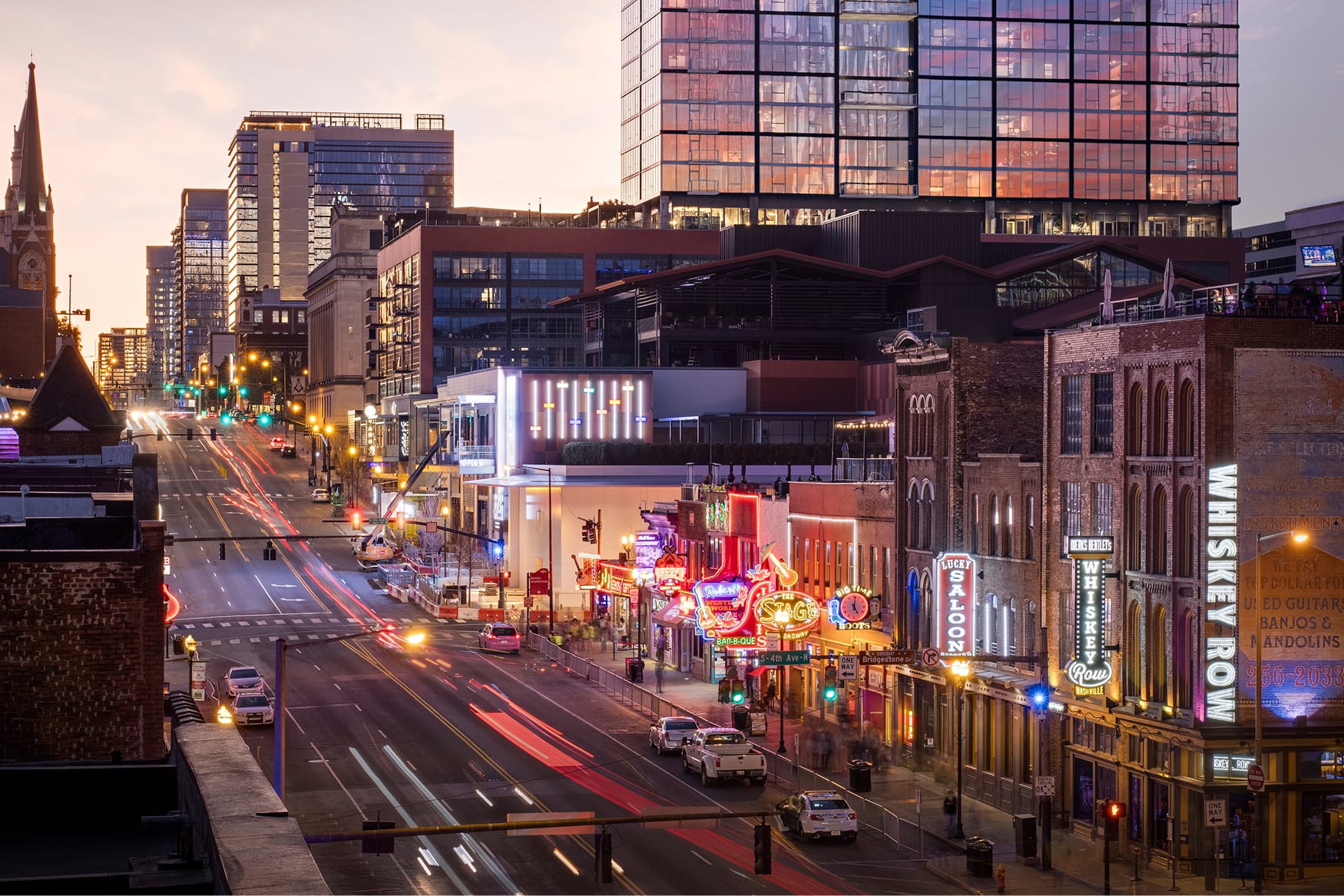 An energized streetscape layers historic architecture with contemporary development, where illuminated signage and nightlife create a distinct sense of place that carries from day into night.