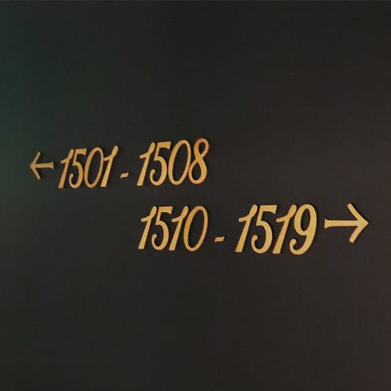 Gold script directional sign reading "1501-1508" and "1510-1519" on a dark wall at The Swexan Hotel - environmental graphic design by RSM Design