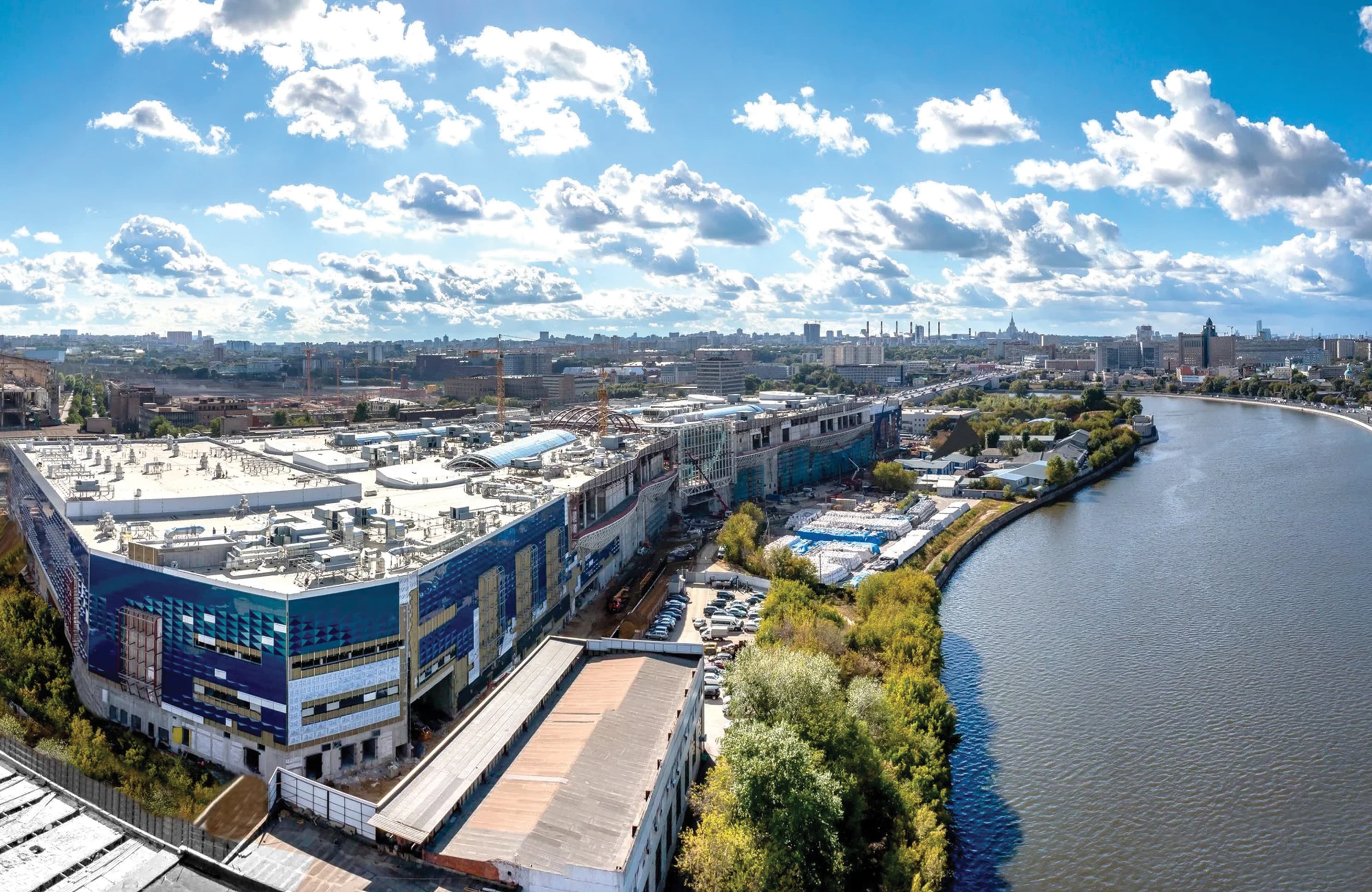 Aerial view of Riviera large-scale international mixed-use retail destination under construction along a riverfront in Moscow, Russia, featuring large-format geometric patterned building facade graphics visible from above — RSM Design environmental graphic design, experiential graphics, specialty graphics, branded environments, and placemaking for retail, mixed-use, waterfront, and international destinations.
